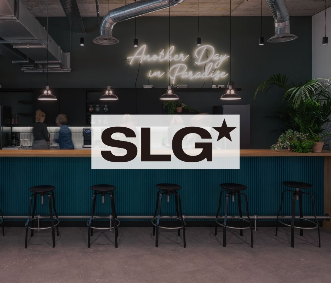 Modern break area at SLG featuring bar seating, industrial lighting, and a neon sign that reads 'Another Day in Paradise,' with plants adding a natural touch