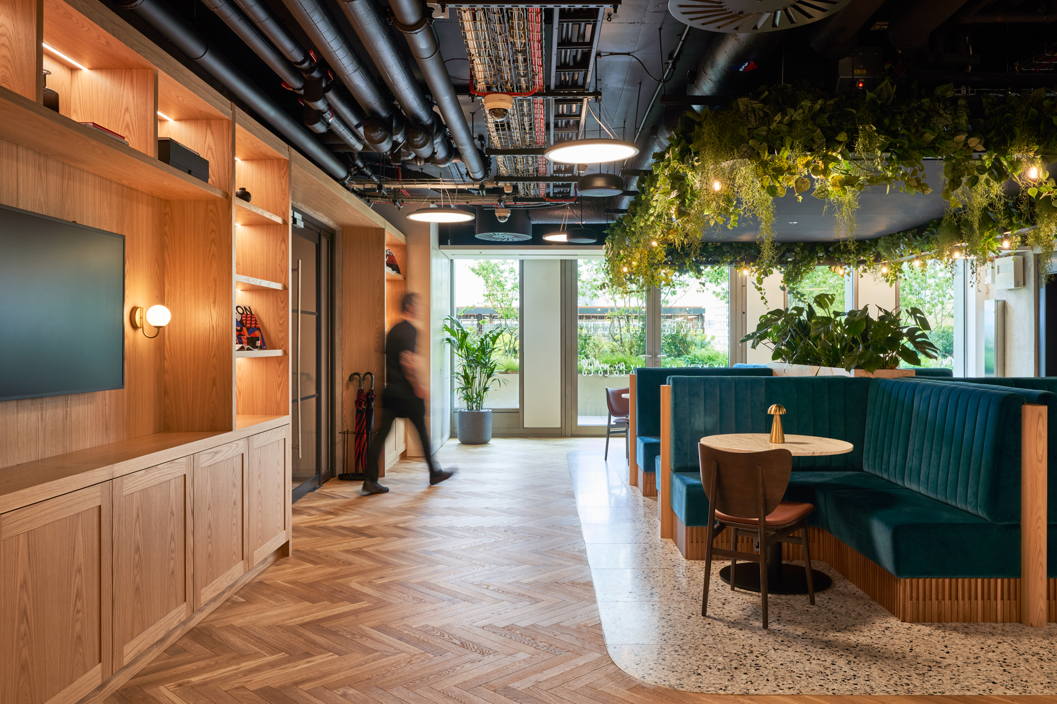 A seating area with teal booths and hanging greenery in the HYLO building. This space blends natural elements with modern design to promote wellbeing and collaboration.