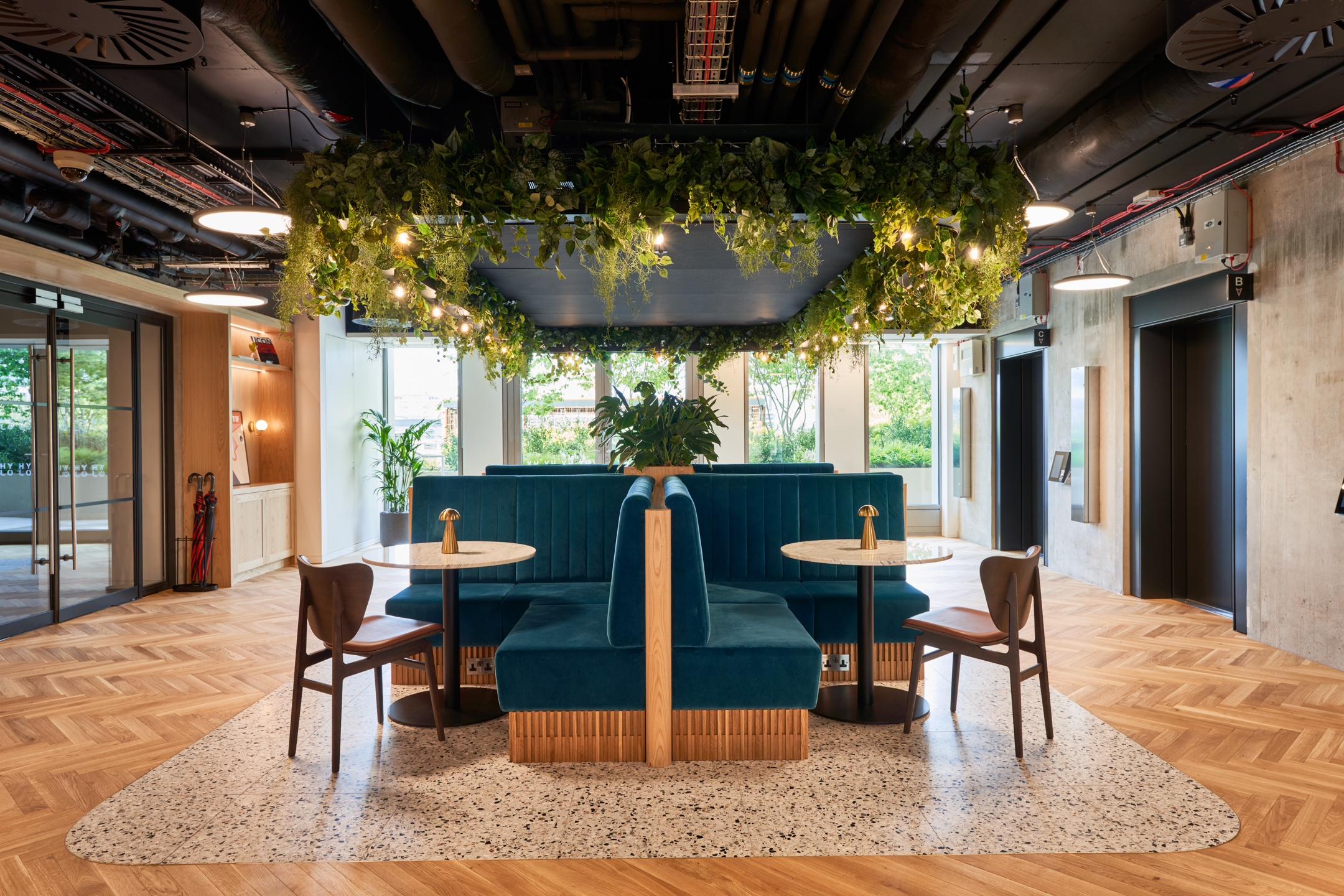 Central seating area with teal booths under a ceiling adorned with greenery in the HYLO building.