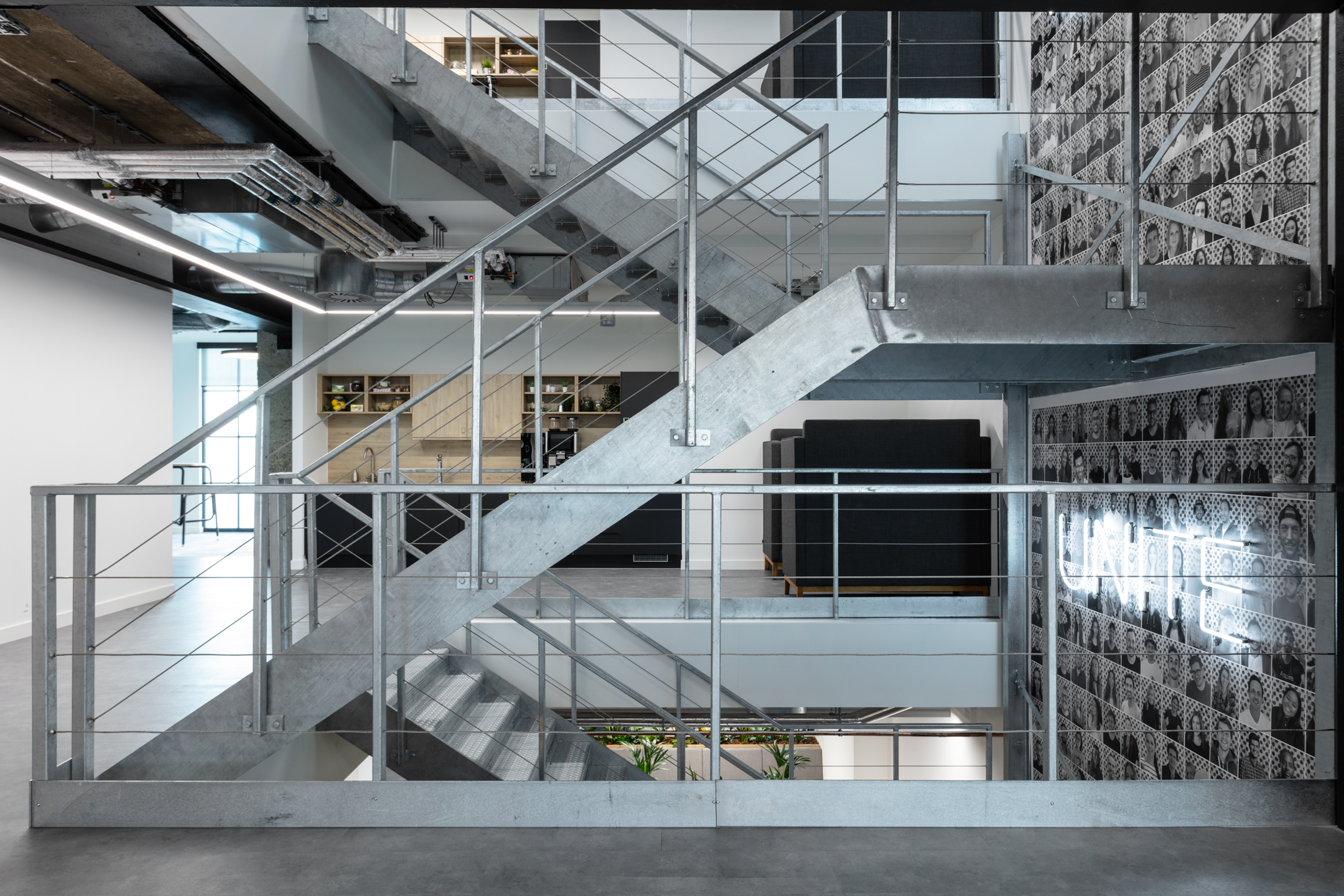 Checkout.com’s metal staircase, ascending alongside a black and white photo wall of headshots with ‘UNITE’ in white LED lights. This project is shortlisted for LCA Awards 2022.