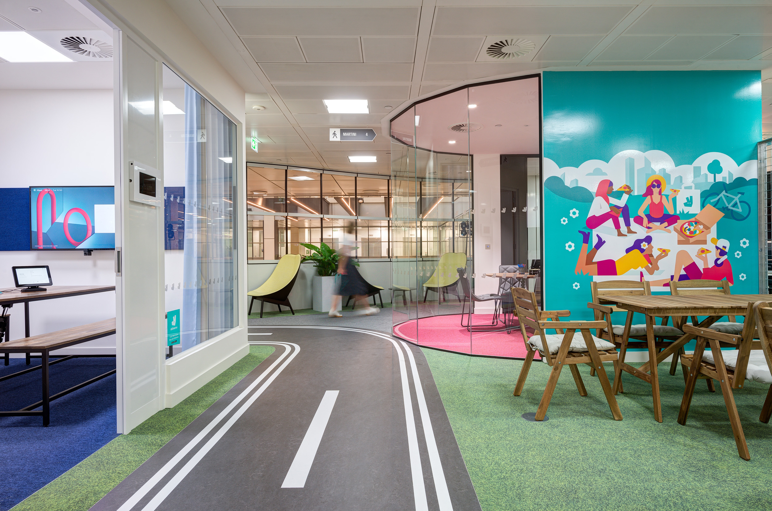 A vibrant relaxation area in the Deliveroo office, with colourful murals, lounge seating, and informal meeting spaces. The space promotes creativity and collaboration among employees.