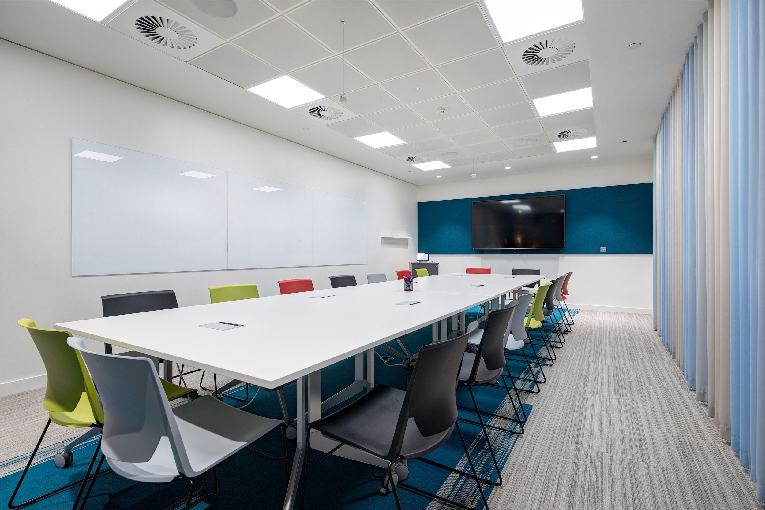 The modern boardroom at Deliveroo’s office, featuring a large table with colourful chairs and a digital screen for presentations.