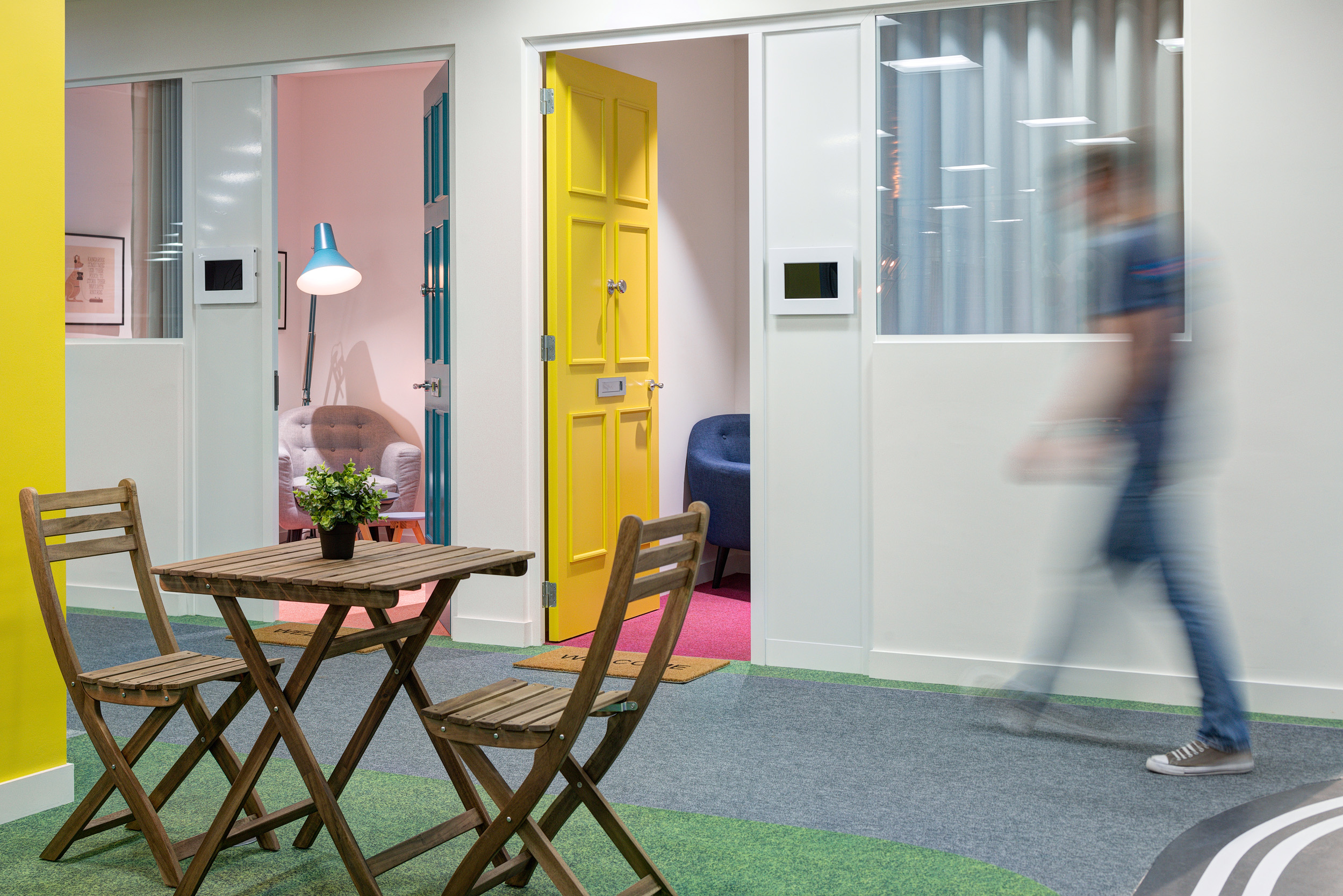 The calming garden room in the Deliveroo office, featuring a picnic-style seating area and colourful doors. This space is designed to enhance employee wellbeing and offer a peaceful retreat.