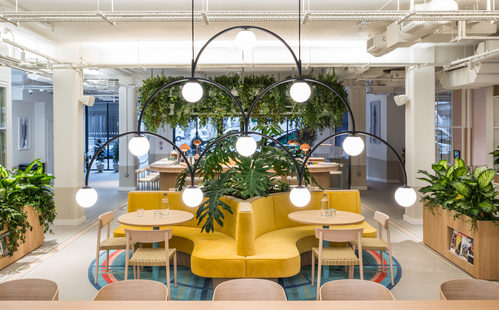 Fora Wells Mews workspace with vibrant yellow seating, modern lighting, and lush greenery.