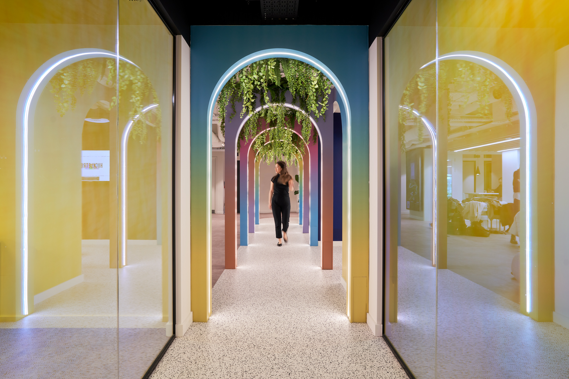 A vibrant corridor at Huckletree, featuring a series of colourful archways with LED lighting and hanging greenery overhead, creating an inviting and modern workspace atmosphere.