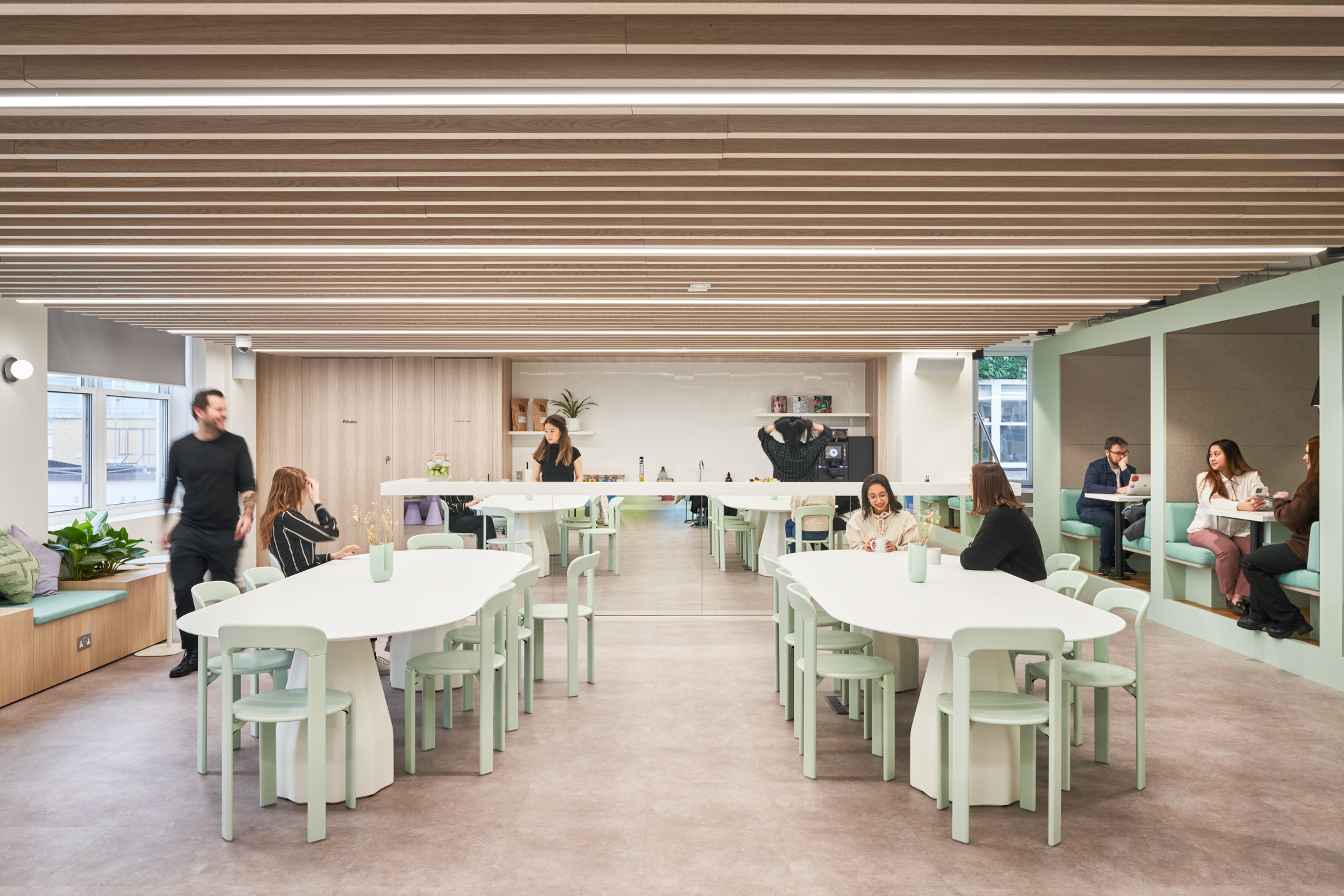 Open communal workspace at Huckletree, featuring modern white tables, pastel chairs, and cosy booth seating, fostering a collaborative and relaxed environment.