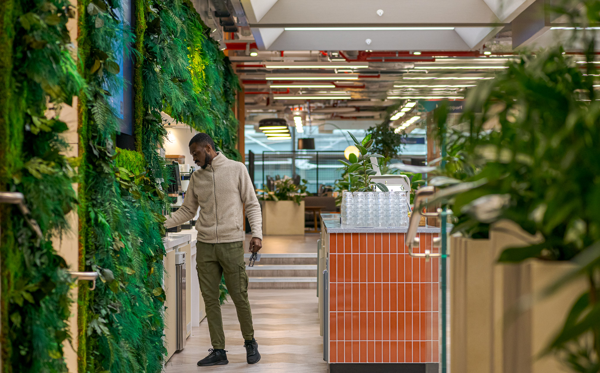 Employee accessing facilities in the vibrant kitchen area of Landsec's 100 Victoria Street Headquarters, designed by Modus Workspace. The area is surrounded by a lush green wall and modern amenities for staff.