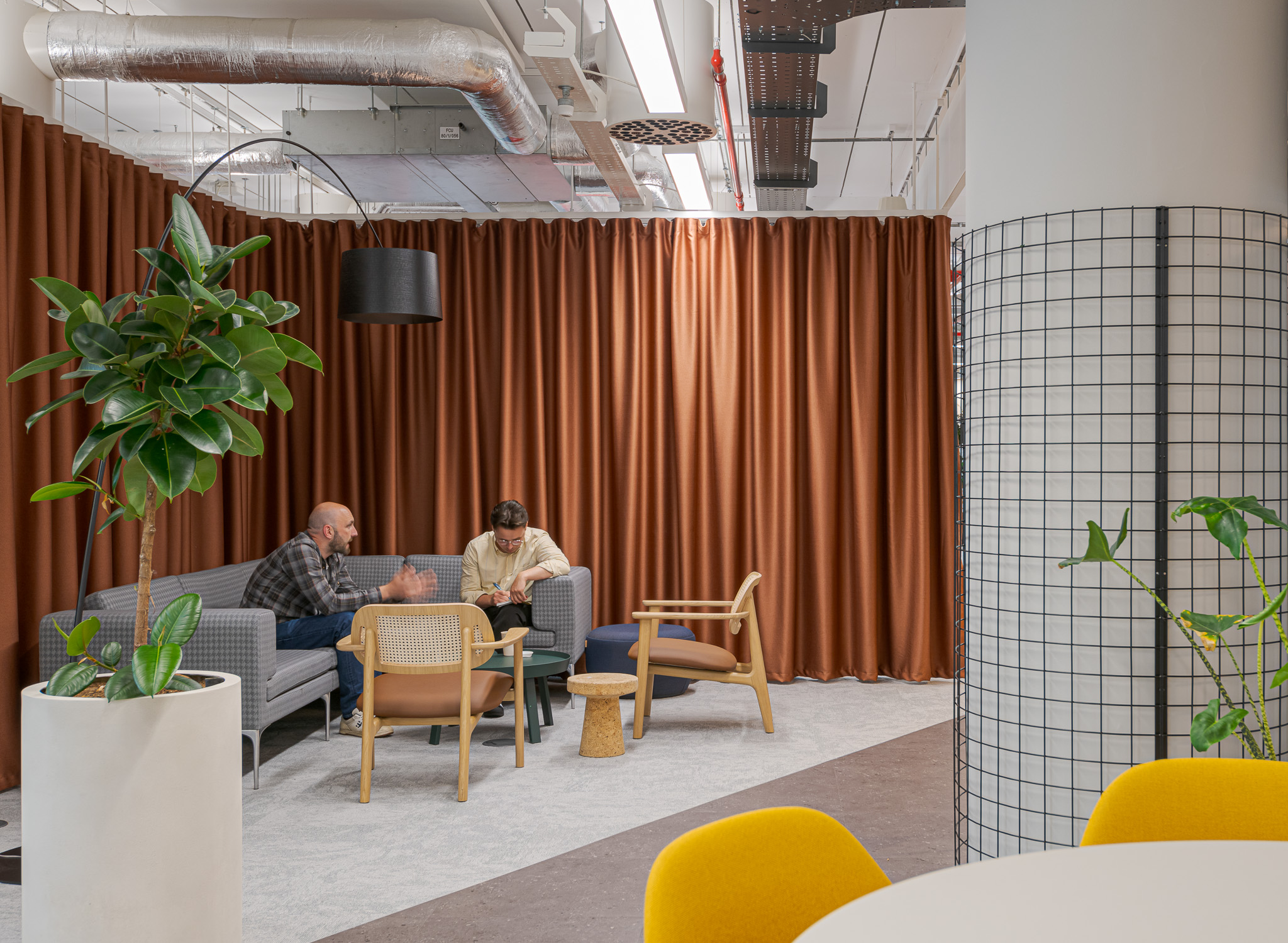 Cozy lounge area in Landsec's 100 Victoria Street Headquarters, designed by Modus Workspace. Two people are engaged in a discussion, utilising the comfortable seating options with warm lighting and contemporary design elements for informal meetings or relaxation