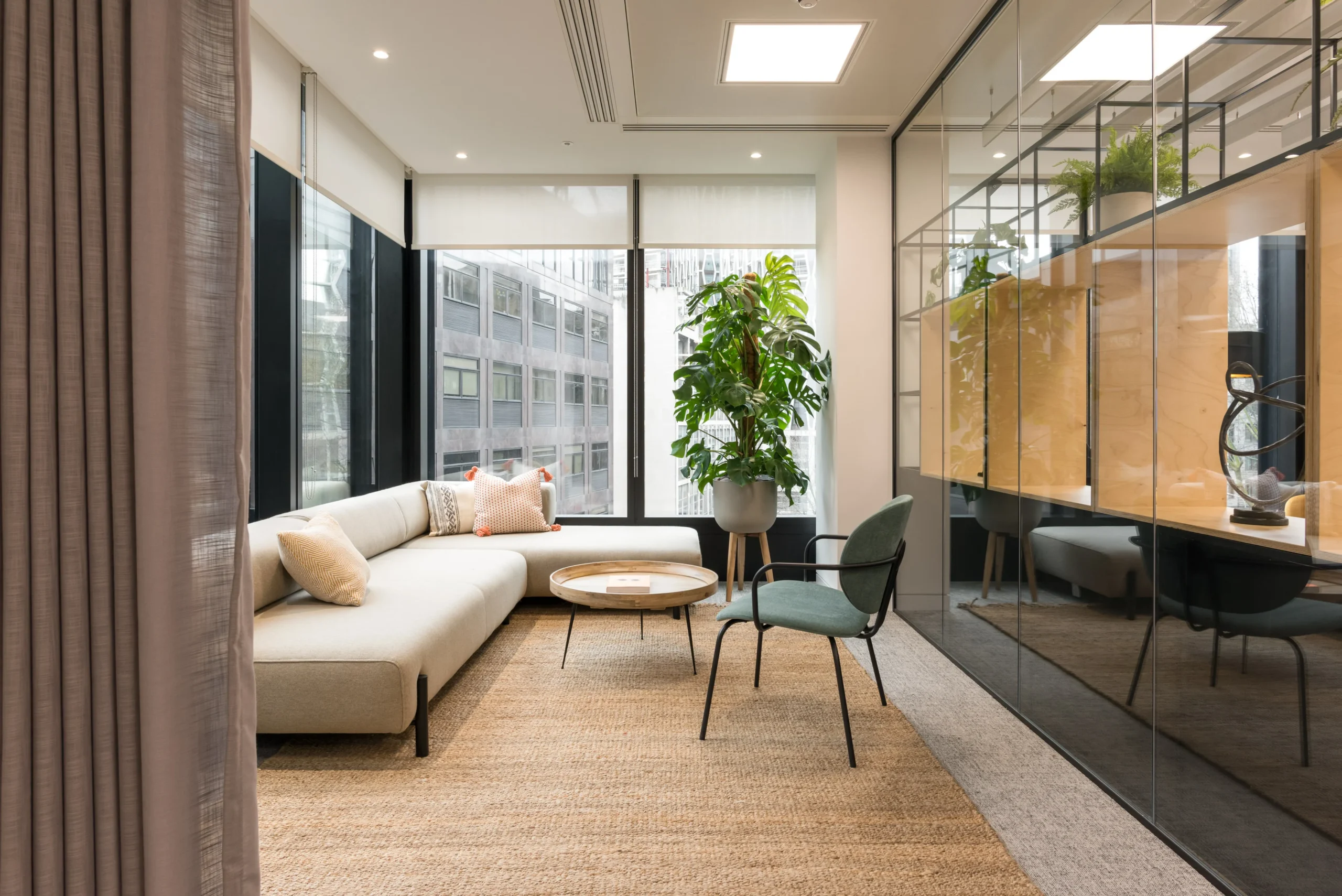 A cozy seating area at London and Oriental, designed by Modus Workspace. The room is furnished with a comfortable sofa, modern chairs, and floor-to-ceiling windows that let in natural light, creating a tranquil environment within the office.