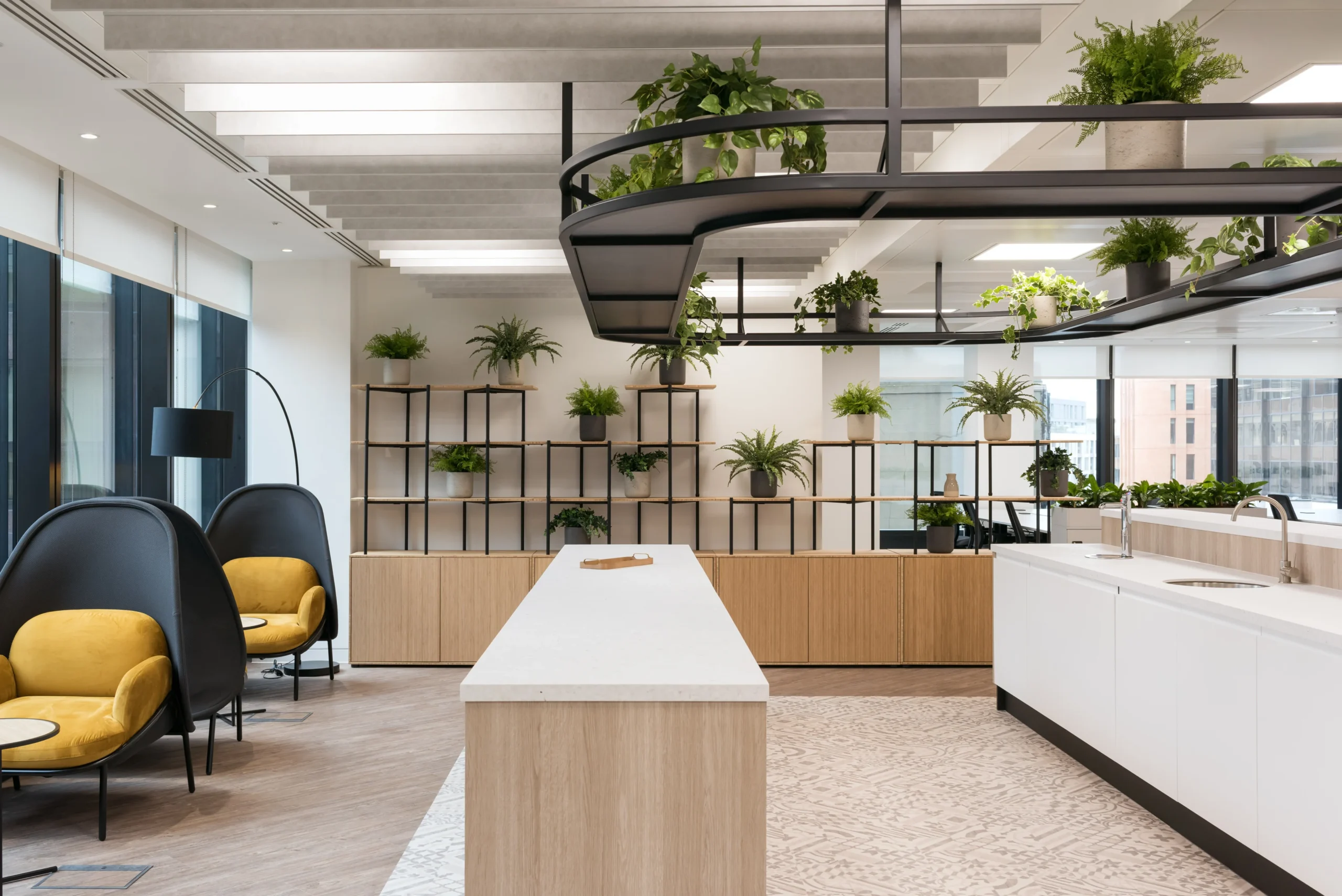 A vibrant office kitchen at London and Oriental, designed by Modus Workspace. The kitchen island is central to the space, surrounded by greenery and modern seating options, fostering a collaborative environment.