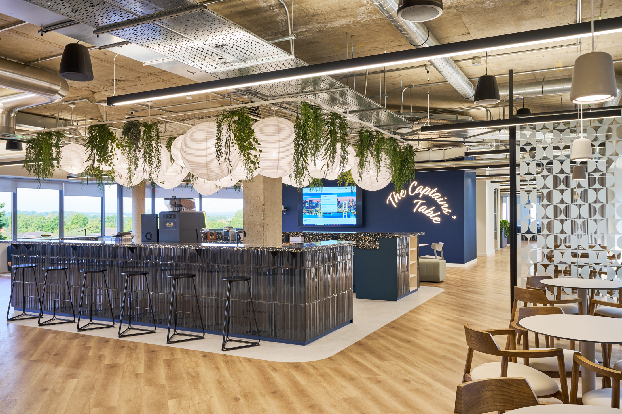 The vibrant bar area at Nomad Foods, featuring hanging greenery and globe lights, is a standout space designed by Modus Workspace to create a dynamic and refreshing atmosphere.