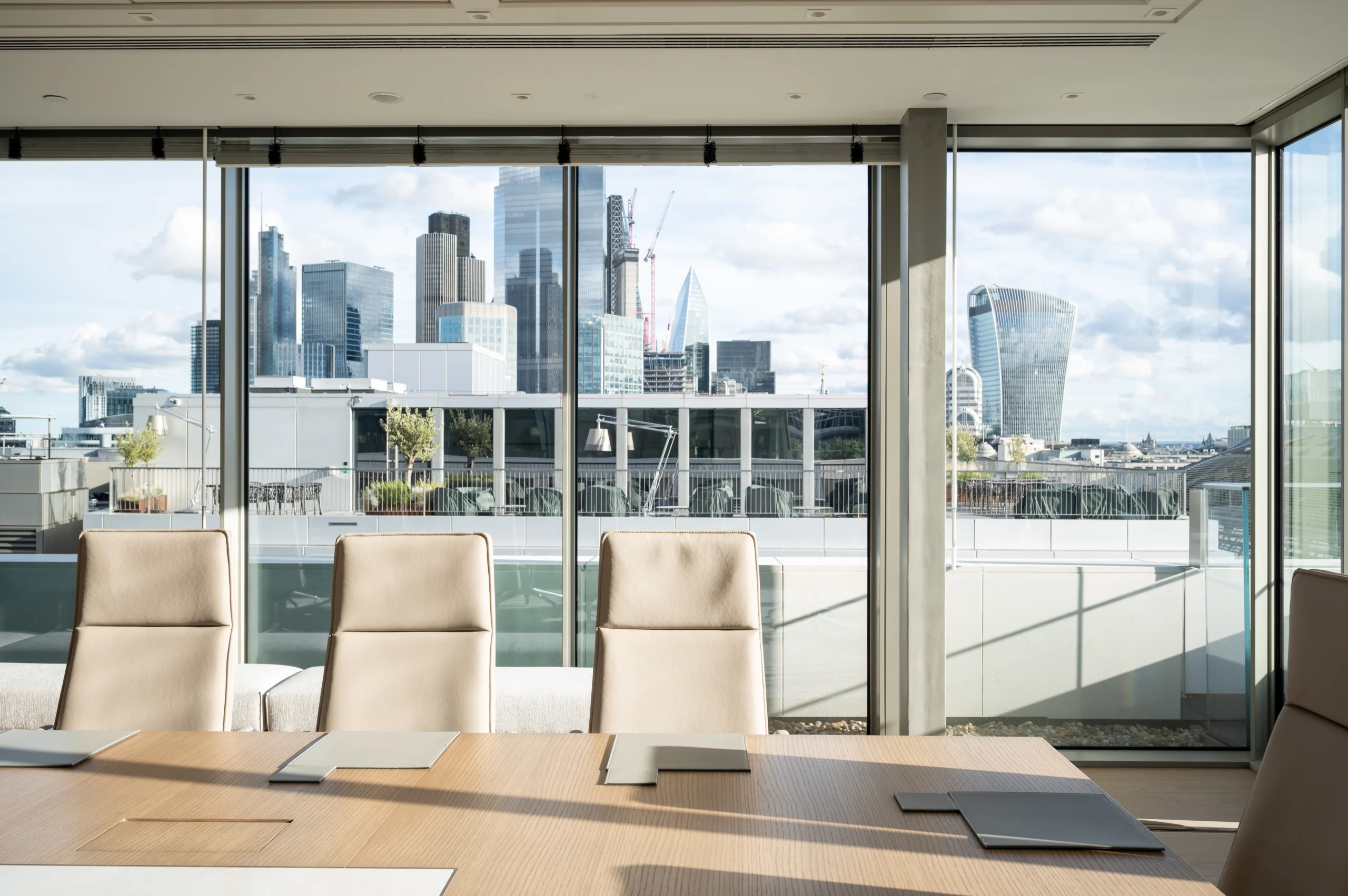 Numis’ modern conference room with a large table and high-backed chairs, surrounded by floor-to-ceiling windows that offer views of the city, including St. Paul's Cathedral. The space is bright and airy, providing an ideal setting for meetings.