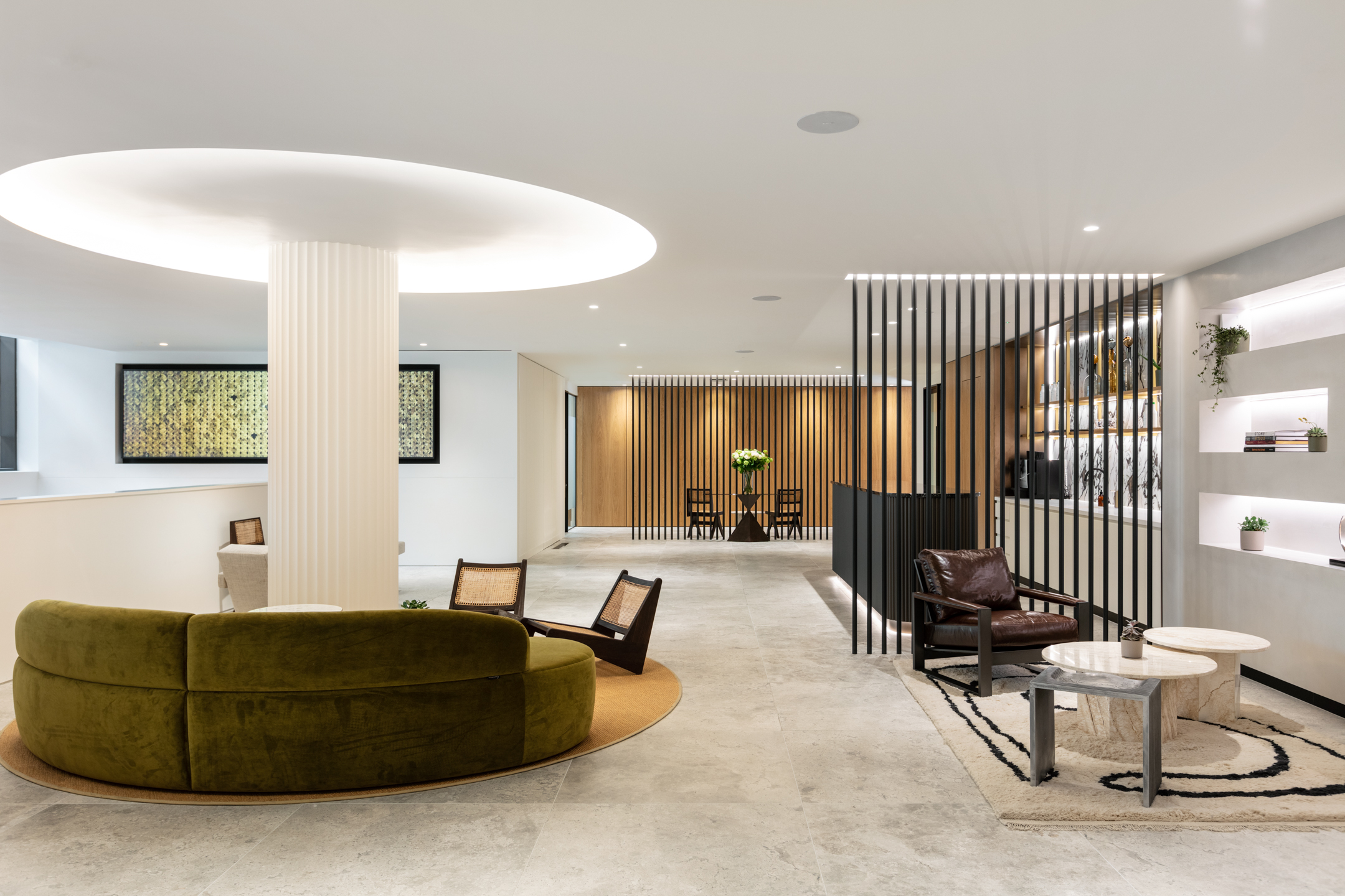 A serene seating area in the Ouronyx aesthetic clinic in Mayfair, designed by Modus Workspace, featuring two plush armchairs and a small marble table. The space is accented by minimalist, backlit shelving and a slatted wood ceiling detail, creating a calm and inviting environment.