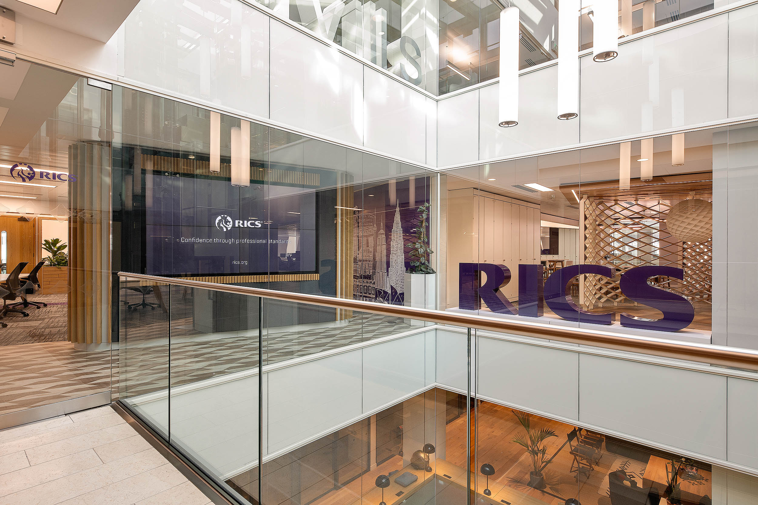 Glass-enclosed reception space at RICS with large purple RICS letters, wood accents, and digital brand displays against a modern office backdrop.