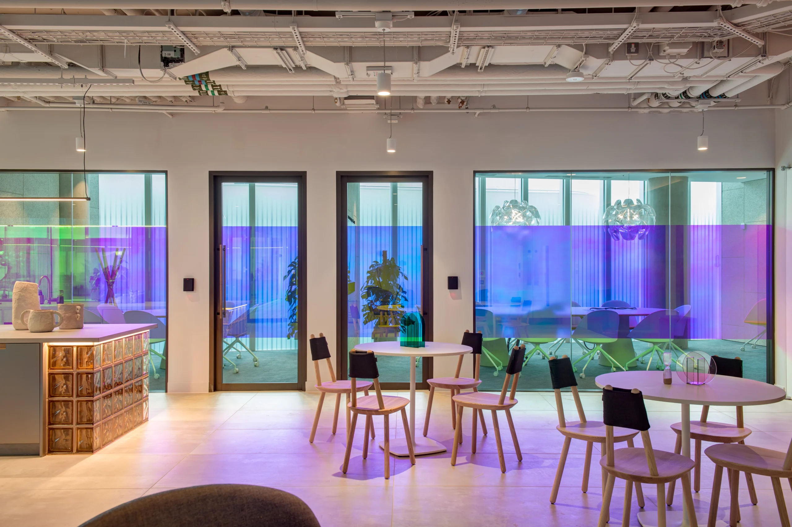 Colourful meeting area at Storey - 2 Kingdom Street, designed by Modus Workspace. This space showcases modern round tables and chairs, accented by vibrant, gradient-tinted glass windows that add privacy and visual interest to meeting rooms.