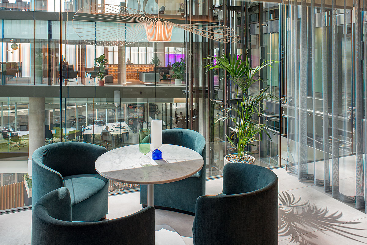 Cosy seating area with a view at Storey - 2 Kingdom Street, designed by Modus Workspace. Green chairs are arranged around a circular marble table, creating an intimate corner for meetings or relaxation while offering a view of the building’s modern interior