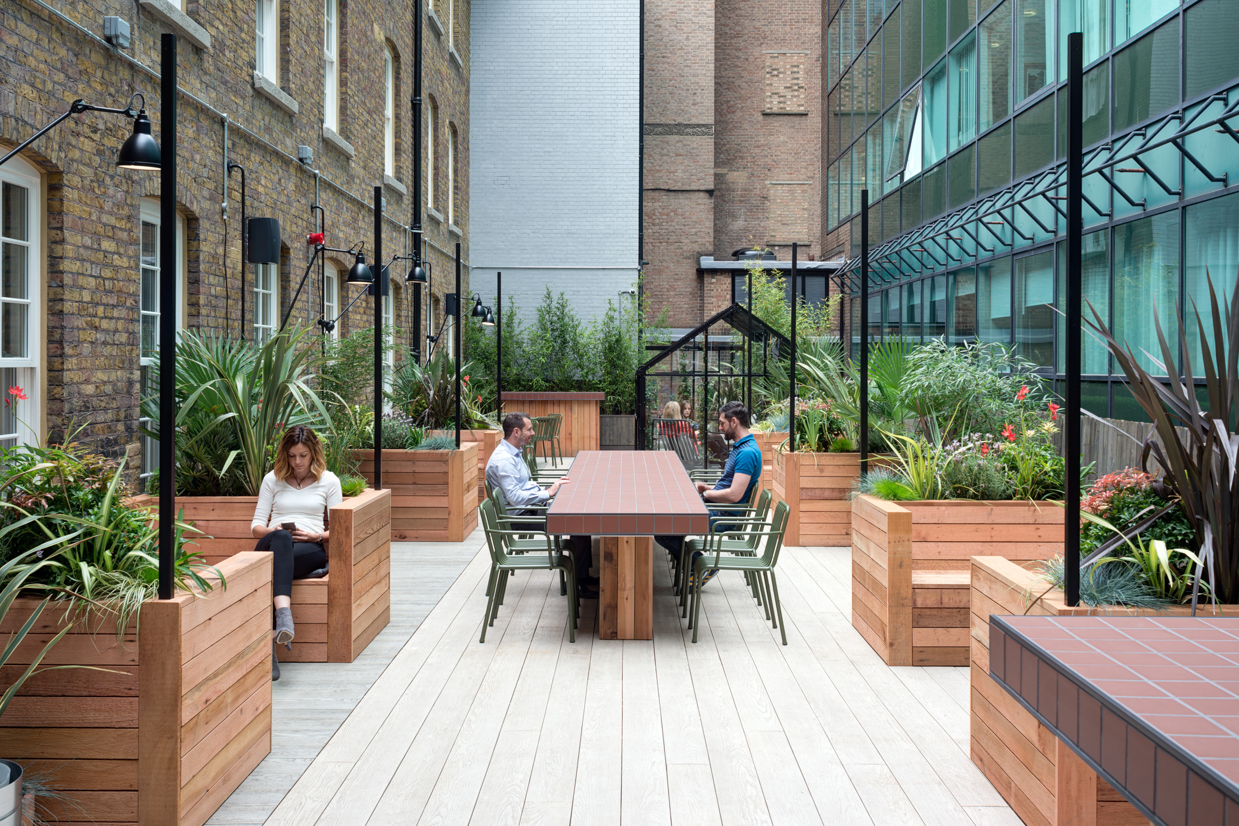 Outdoor terrace at The Office Group Wimpole Street, designed by Modus Workspace, offering a tranquil area with greenery and benches. Employees are seated at a long wooden table working on laptops, enjoying the fresh air.