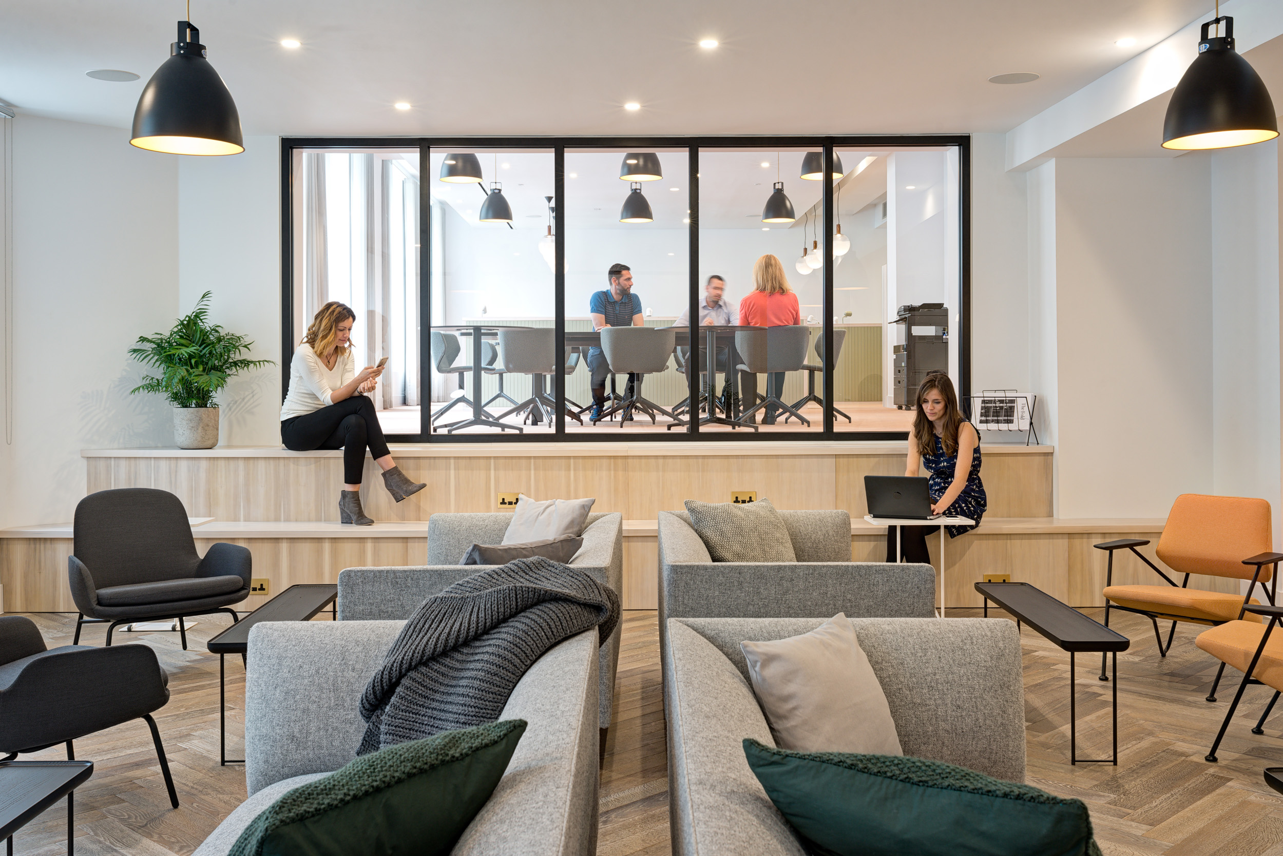 A seating area with a view into a glass-walled collaborative workspace at The Office Group Wimpole Street, designed by Modus Workspace. Individuals are seated, working, and in discussion, adding a dynamic atmosphere to this modern workspace.