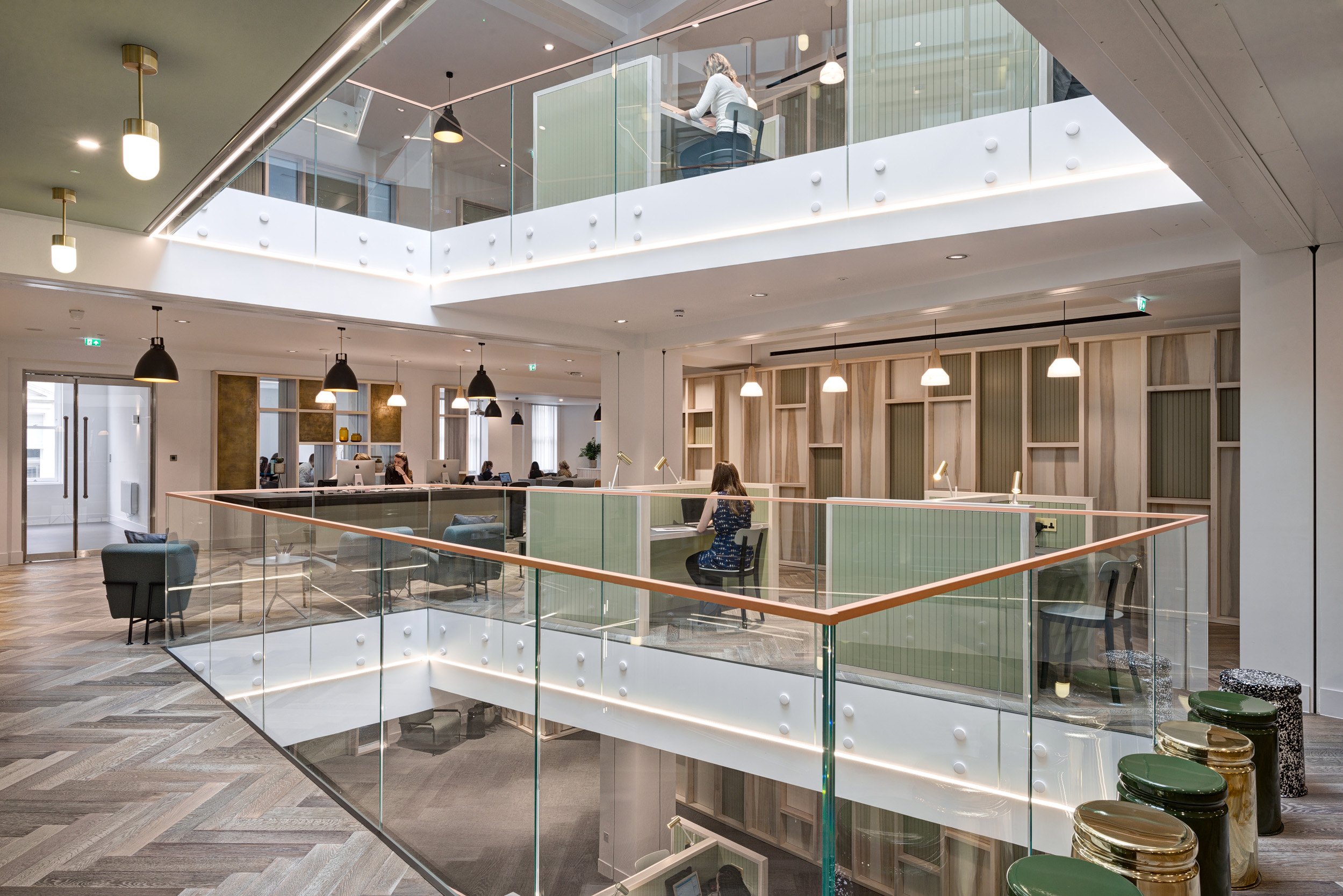 A bright, airy atrium at The Office Group Wimpole Street, designed by Modus Workspace. Workers are seated at desks on both levels, taking advantage of the open, collaborative environment and natural light filtering through.