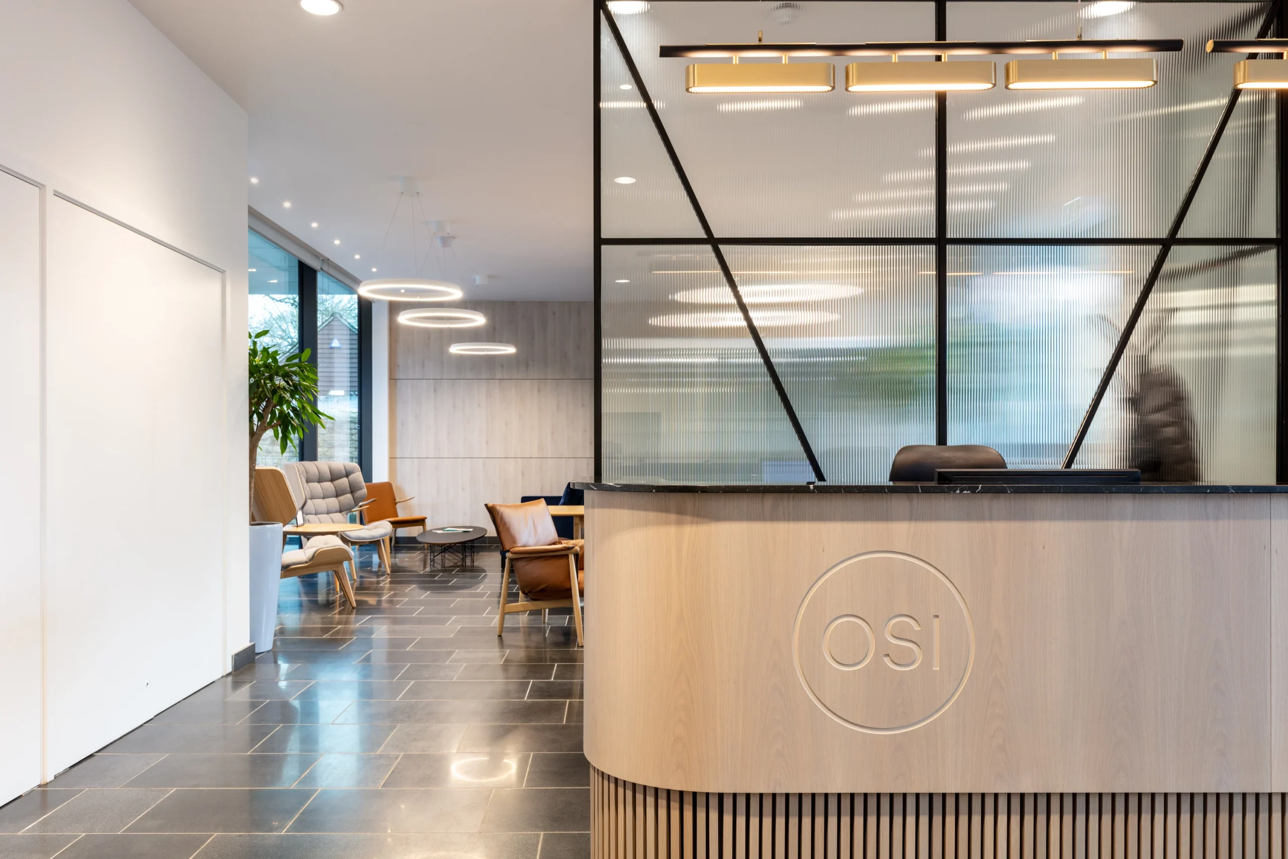 OSI’s modern reception area featuring a wooden reception desk with the logo 'OSI,' a geometric glass partition, and a seating area with contemporary chairs and circular pendant lights in the background.