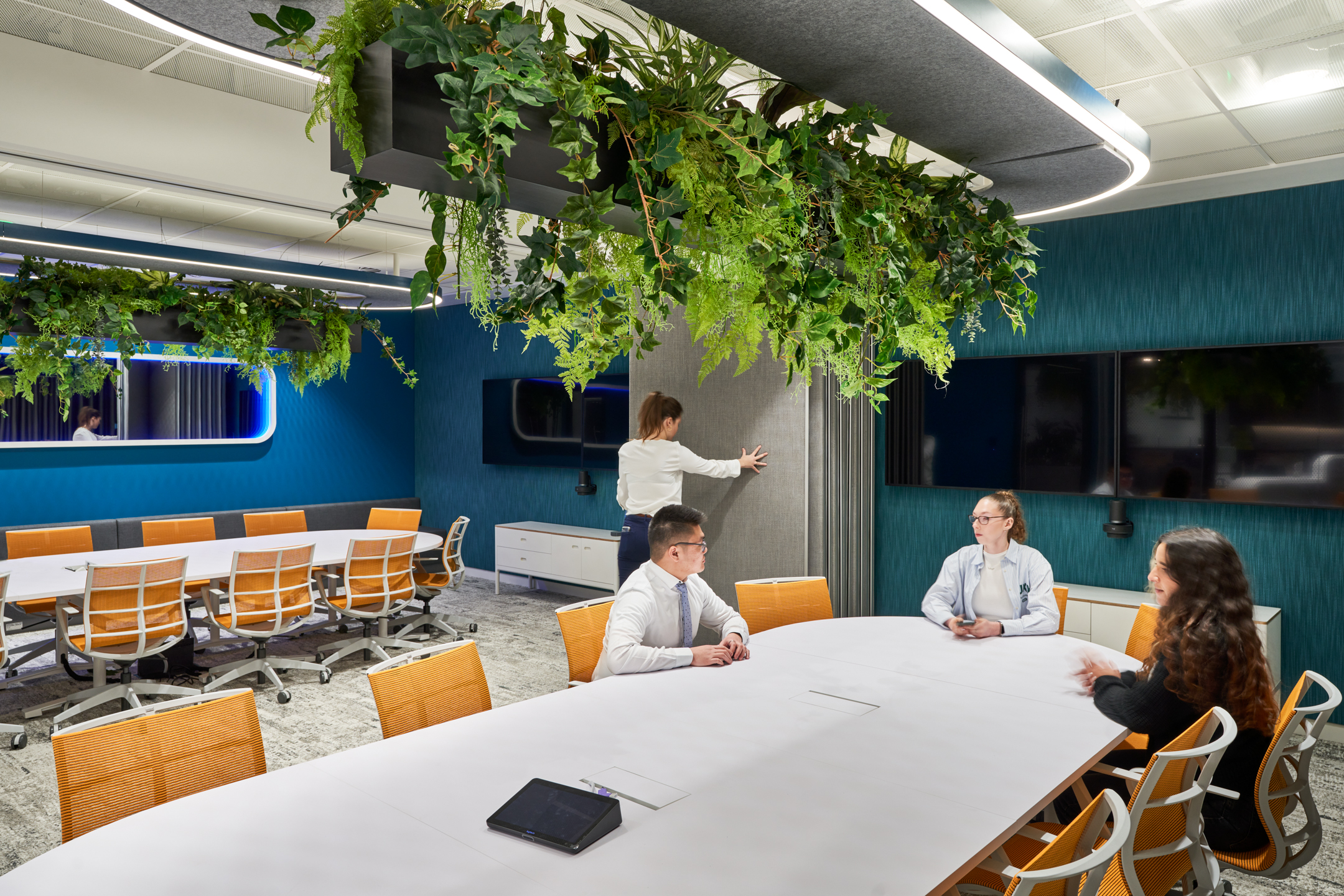 Blue themed meeting room with orange mesh office chairs, and a hanging plant ceiling installation.