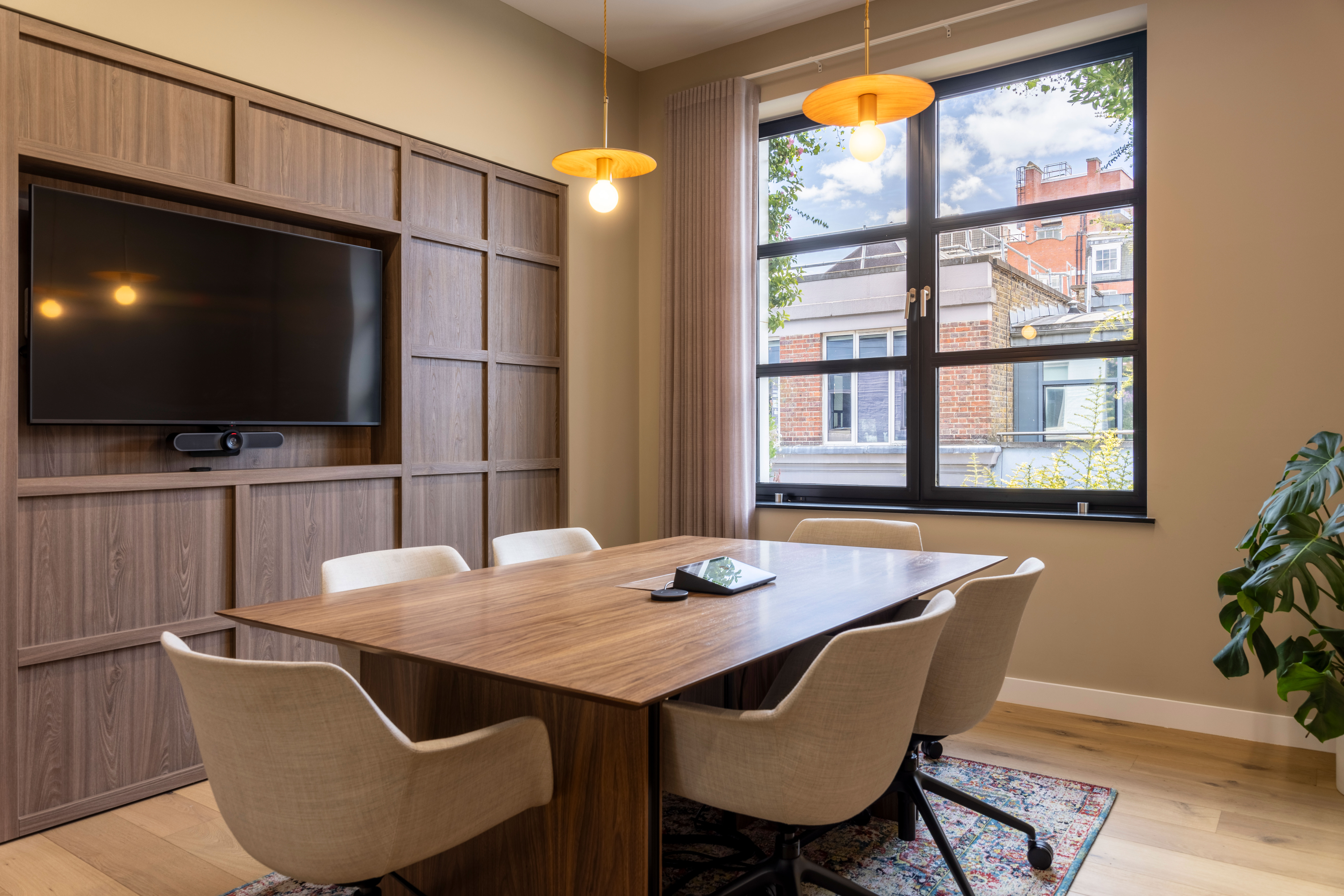 A meeting room in Transition’s London office featuring a wooden table, upholstered chairs, built-in cabinetry with an AV screen, and large windows offering natural light.