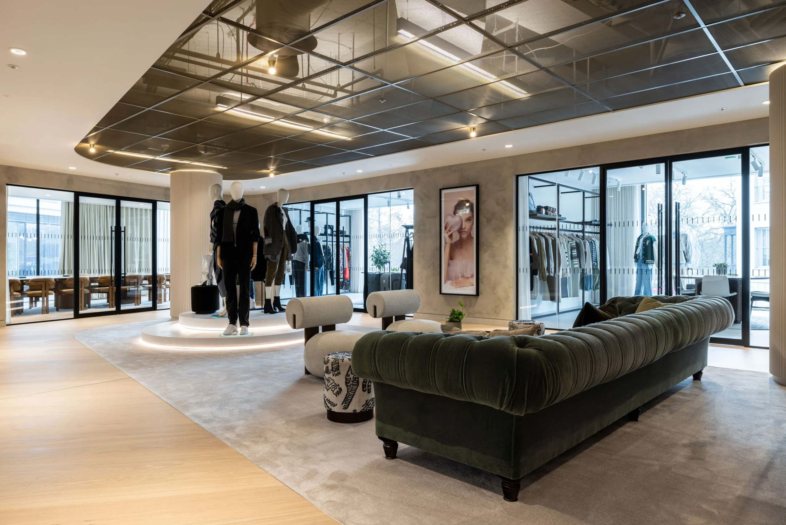 A spacious lounge area at Authentic Brand Group, designed by Modus, with mustard-coloured armchairs, a large ottoman, and open-plan workstations in the background, highlighted by modern lighting and greenery.