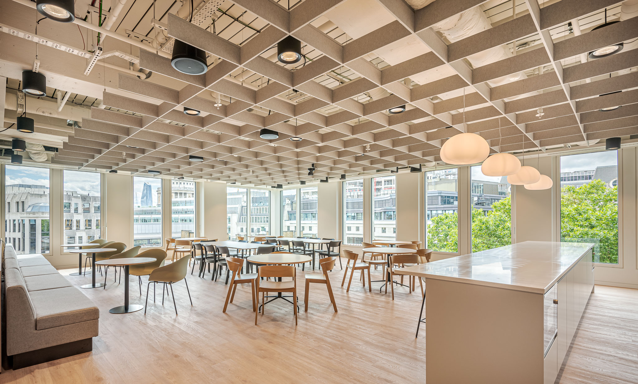 A bright and spacious teapoint seating area at the Bank of Ireland, designed by Modus Workspace, with wood furniture and ceiling decor with views of the London cityscape.