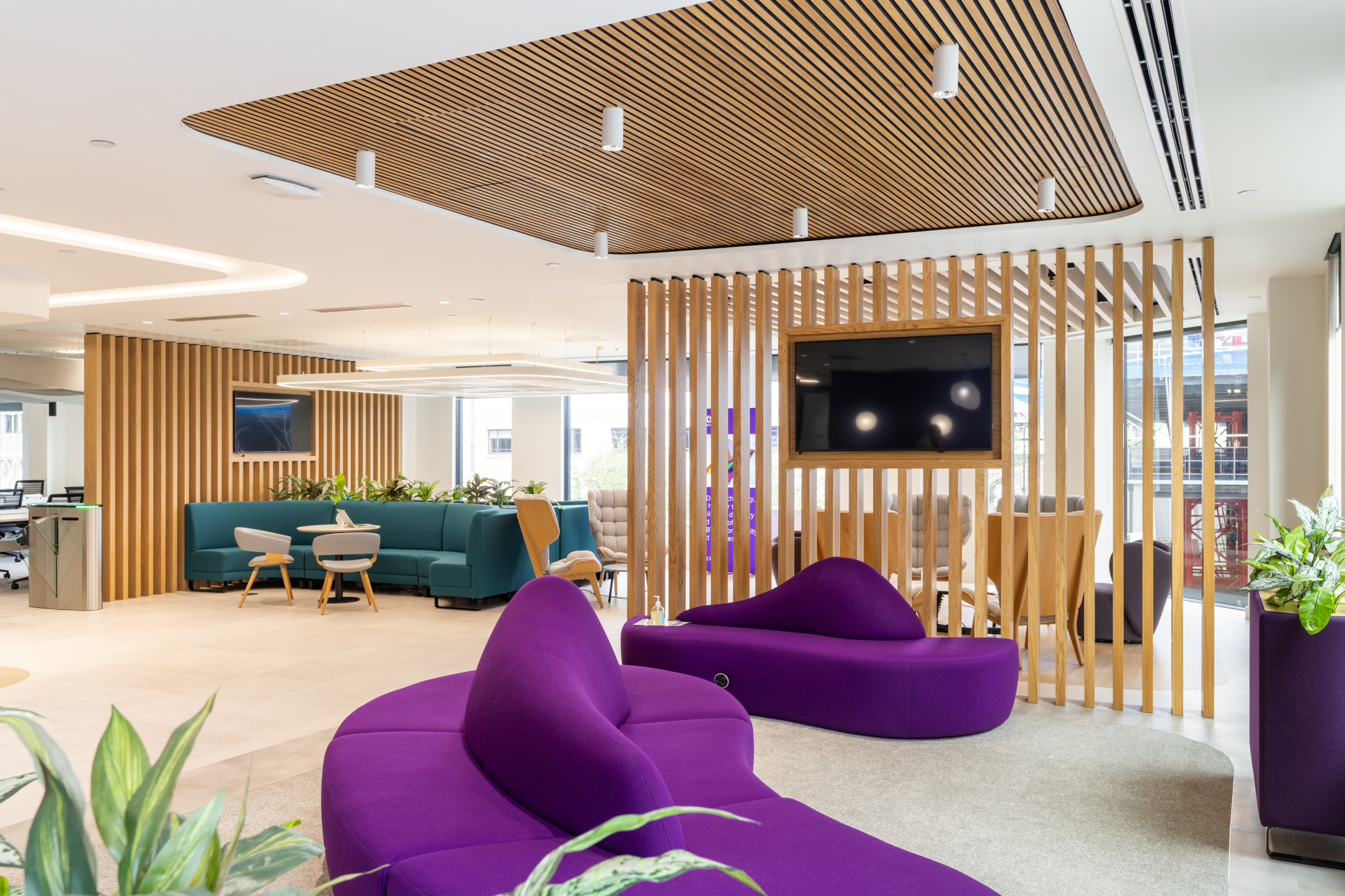 A stylish breakout area at DXC Technology with vibrant purple seating, teal sofas, and a wooden slatted divider creates a relaxing atmosphere.