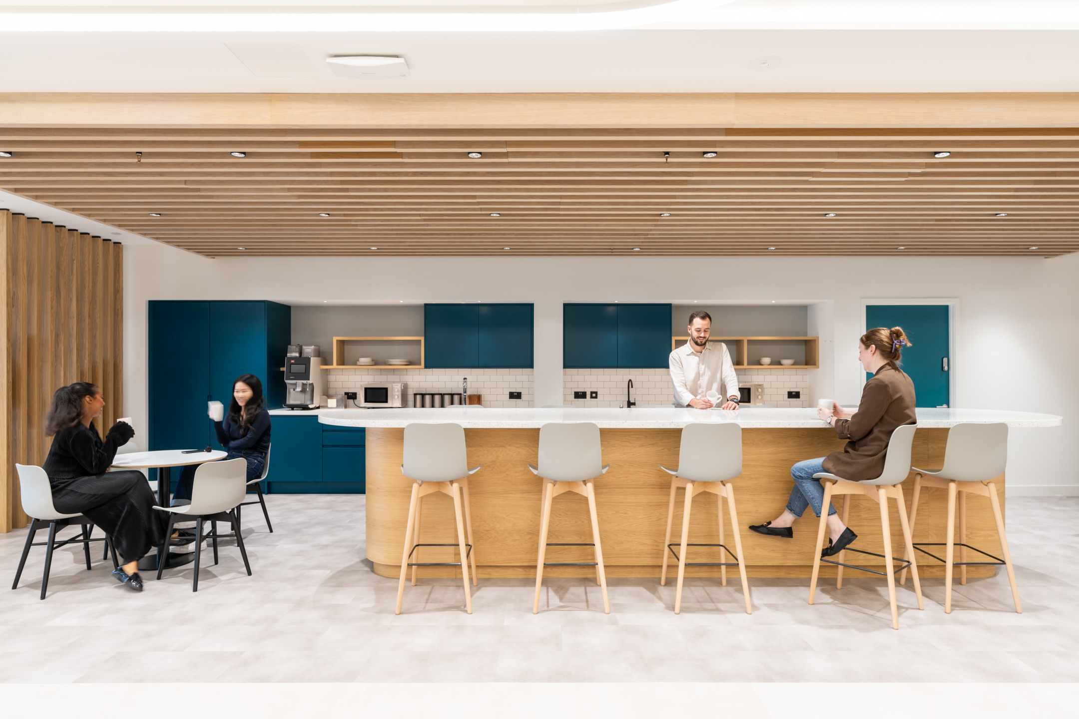 A kitchen area at DXC Technology with a spacious island, high stools, teal cabinets, and employees engaging in casual conversation.