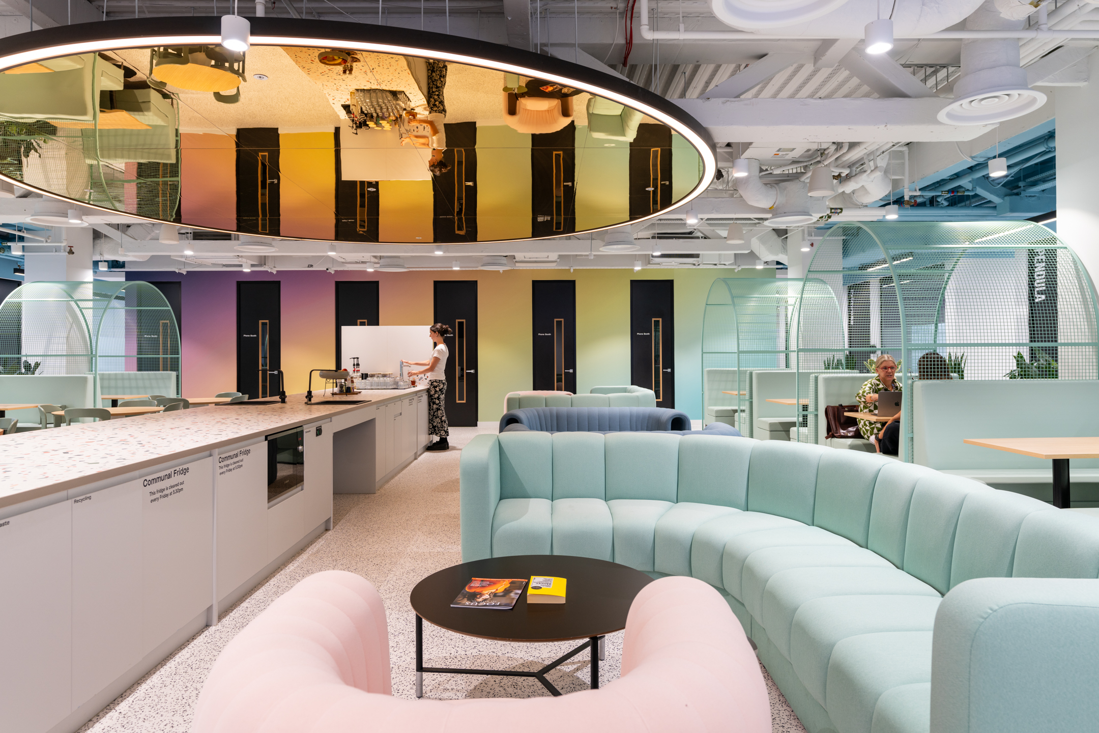 A vibrant workspace at Huckletree Bishopsgate featuring pastel-coloured sofas and a modern teapoint area with a mirrored ceiling and communal countertops.