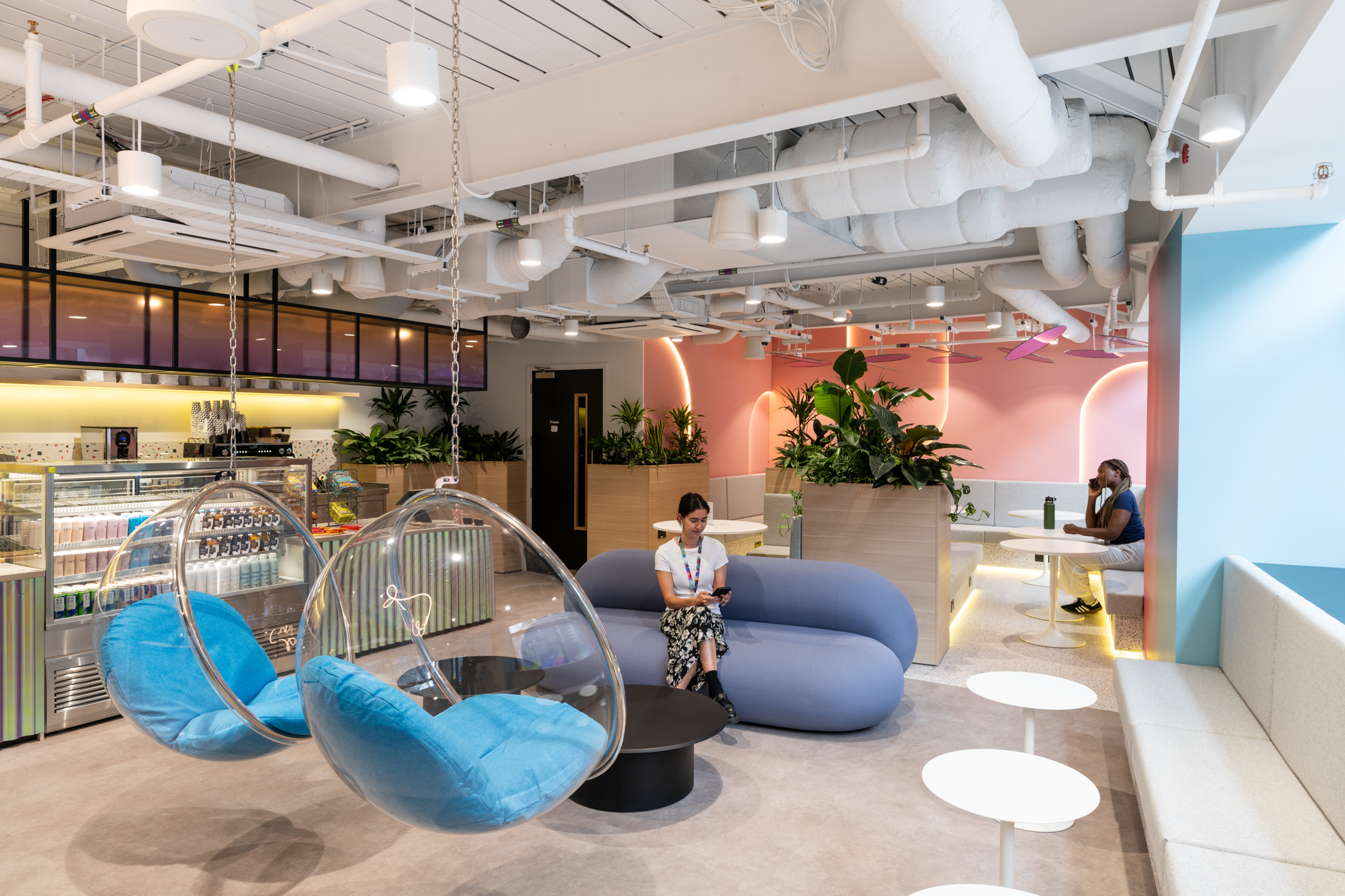 Breakout area at Huckletree Bishopsgate with bubble chairs, pastel blue seating, and a café counter in the background under warm lighting.