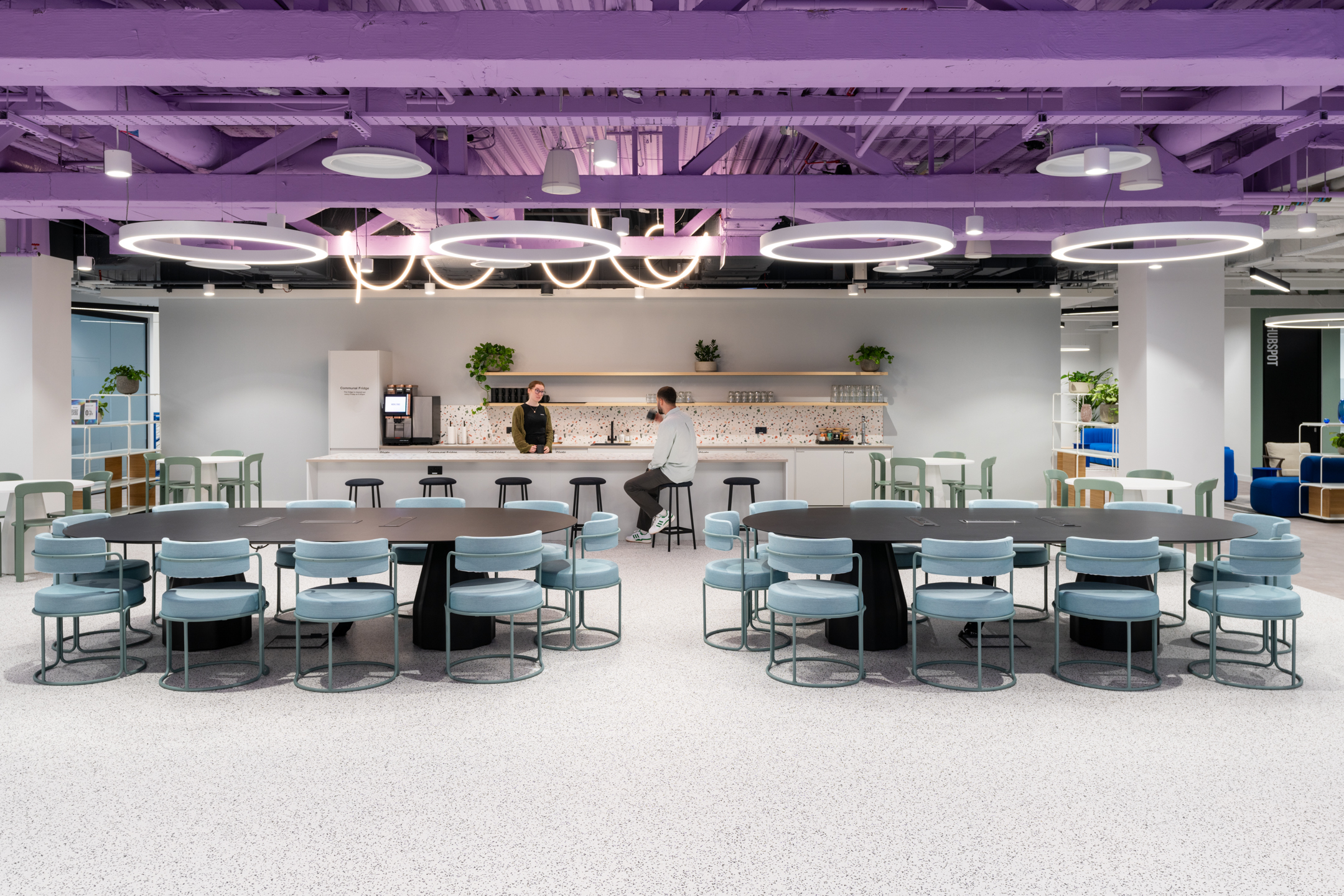 Spacious teapoint space at Huckletree Bishopsgate, with seating areas, a long dining table, and a purple ceiling.