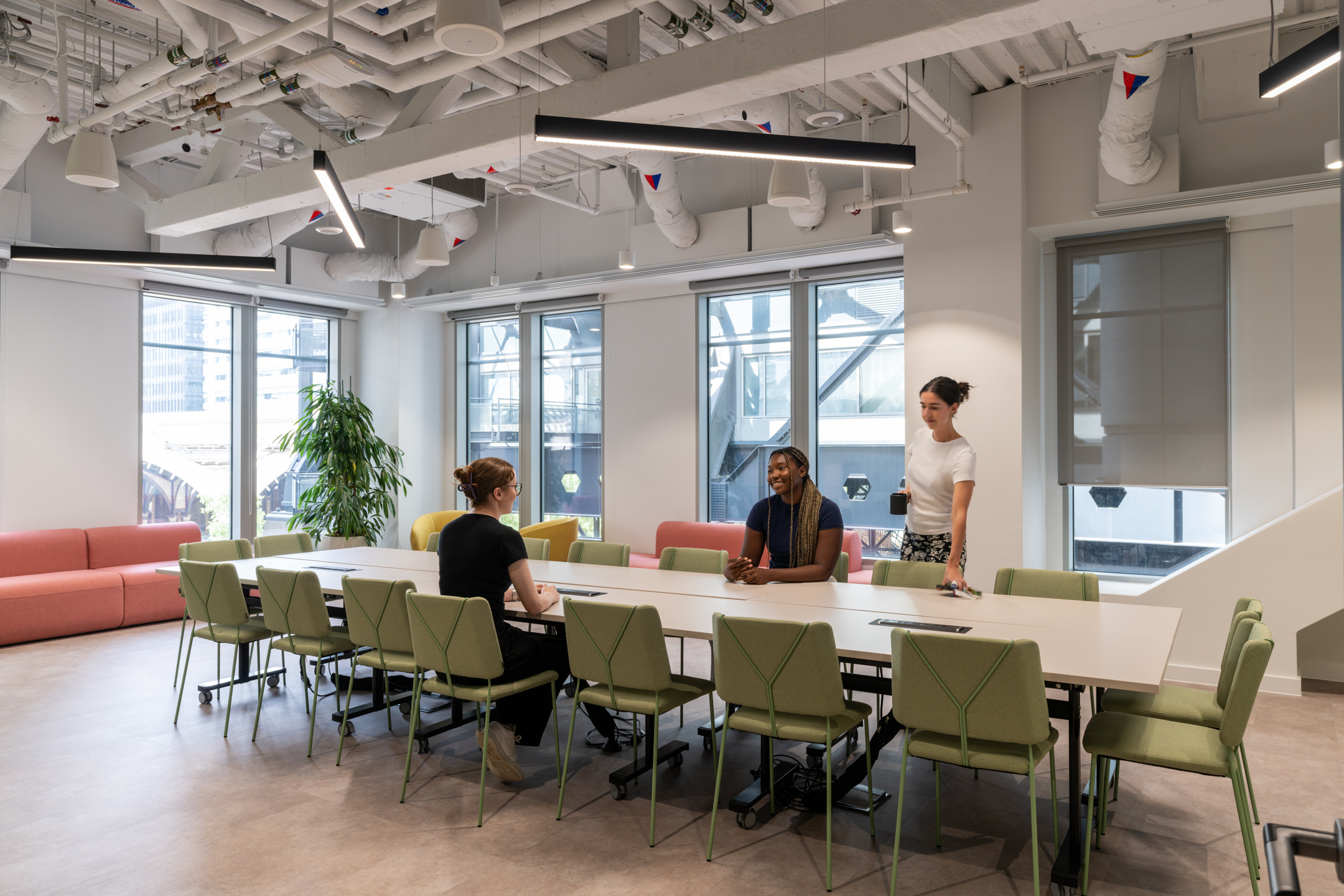 A meeting room at Huckletree Bishopsgate, with green chairs and a large table surrounded by windows.