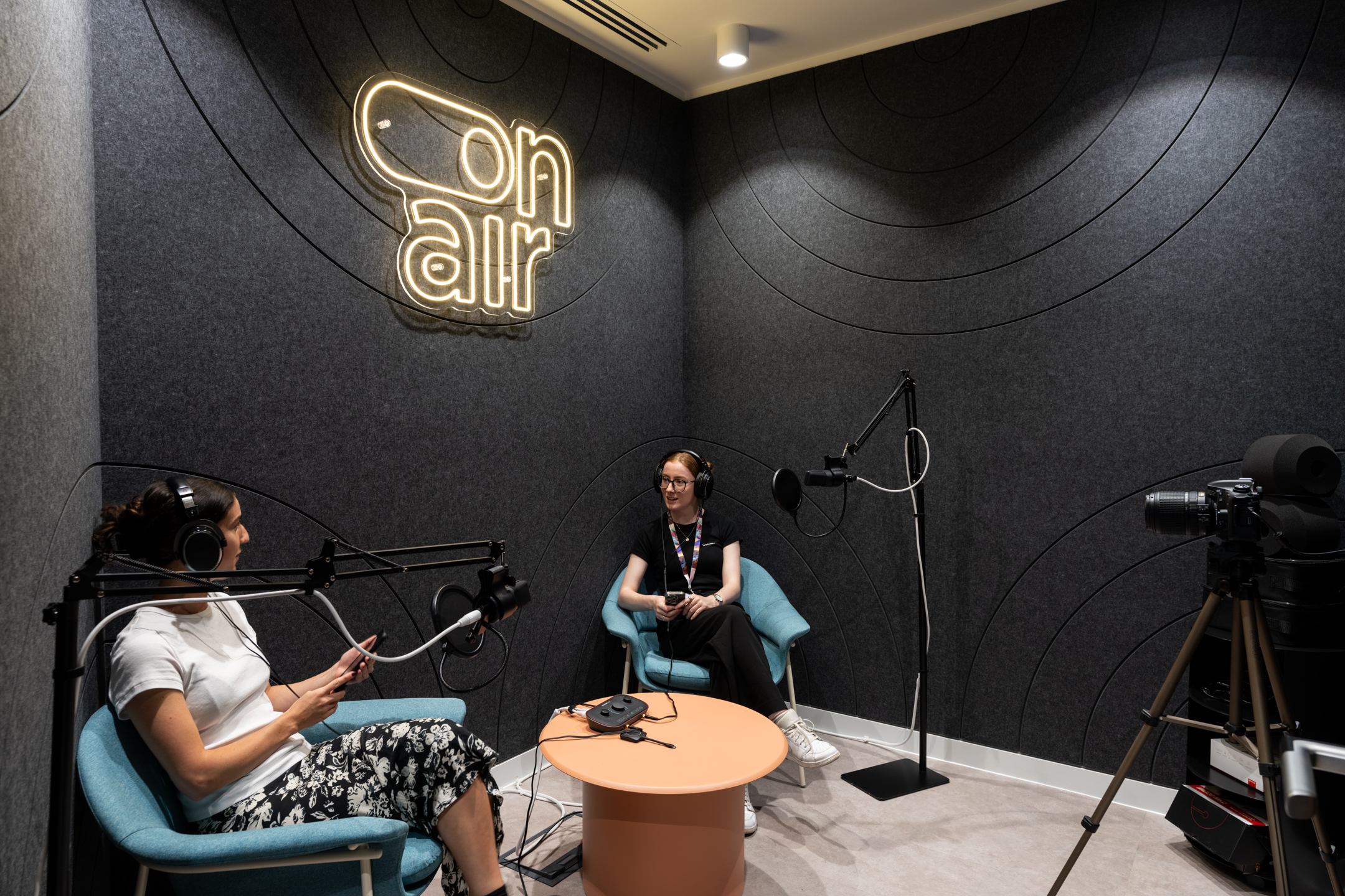 The recording studio at Huckletree Bishopsgate, equipped with two chairs, a round table, podcast microphones, and a neon “On Air” sign on the wall.