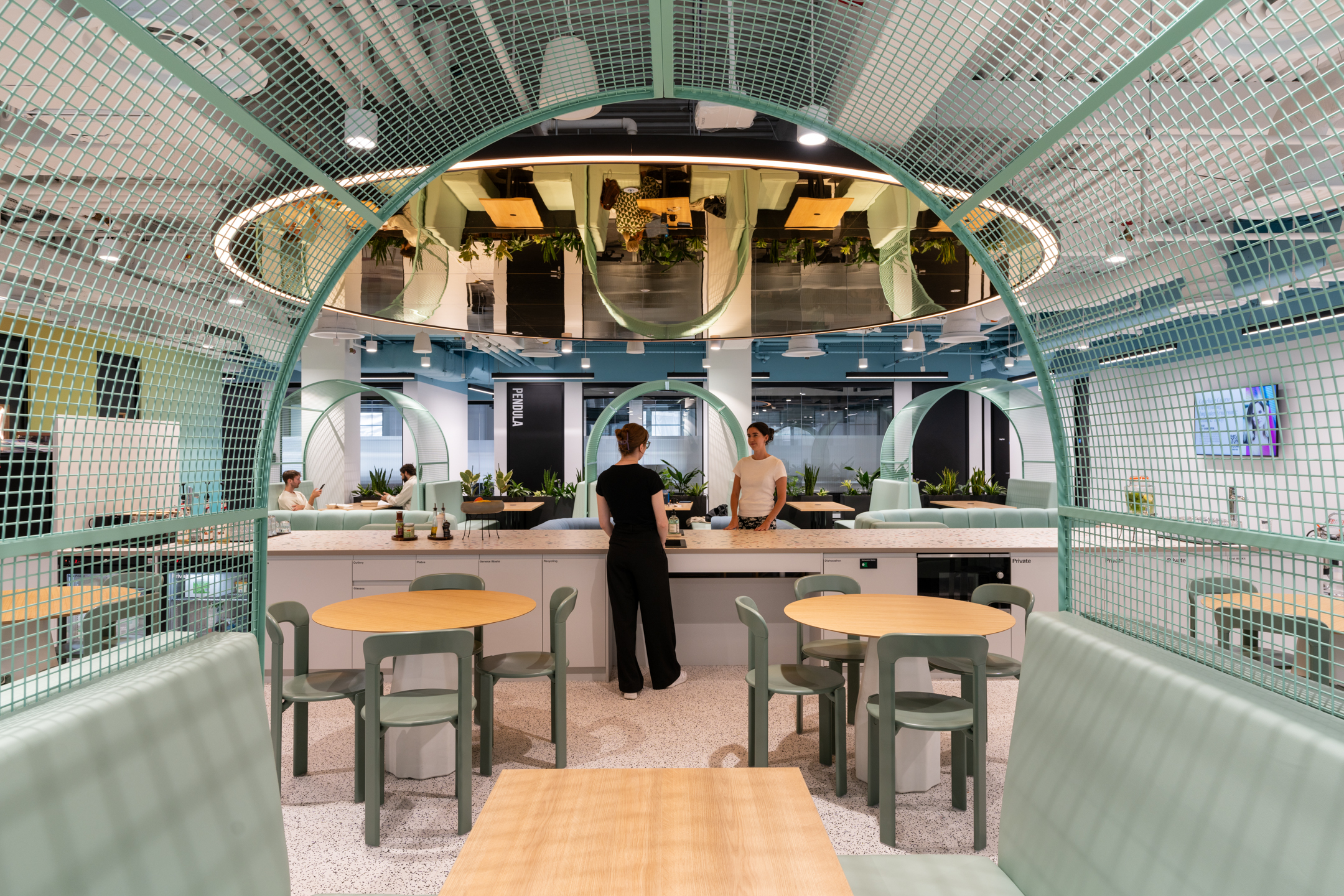 Private booths at Huckletree Bishopsgate are designed with green mesh partitions and seating next to the teapoint area with a modern industrial look.