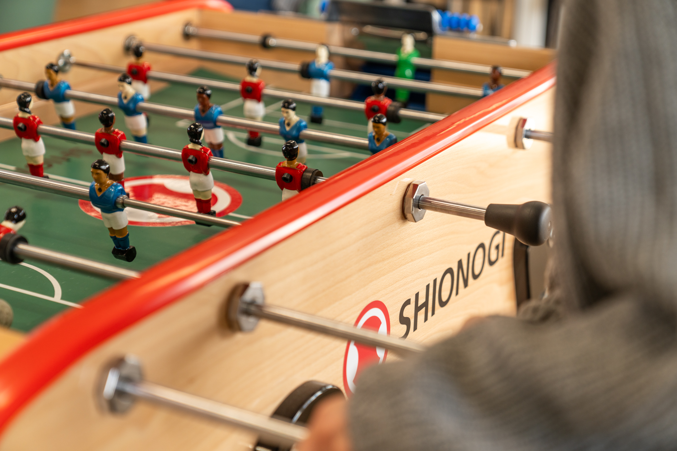 Close-up of a Shionogi-branded foosball table with red and blue players.