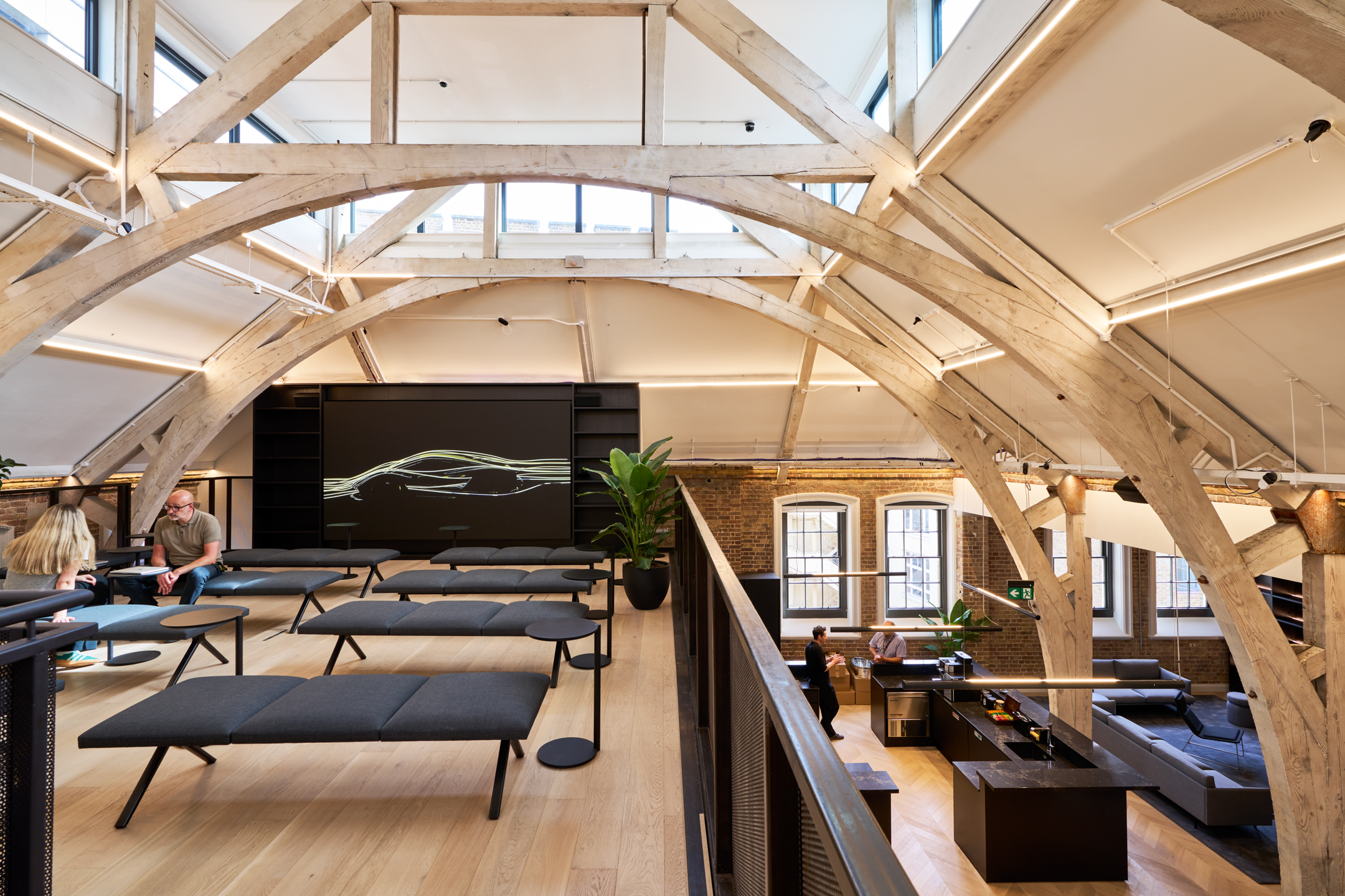 The bright upper floor of Lotus's new headquarters, designed by Modus, featuring exposed wooden beams and minimalist seating under the arched roof of the Ragged School.