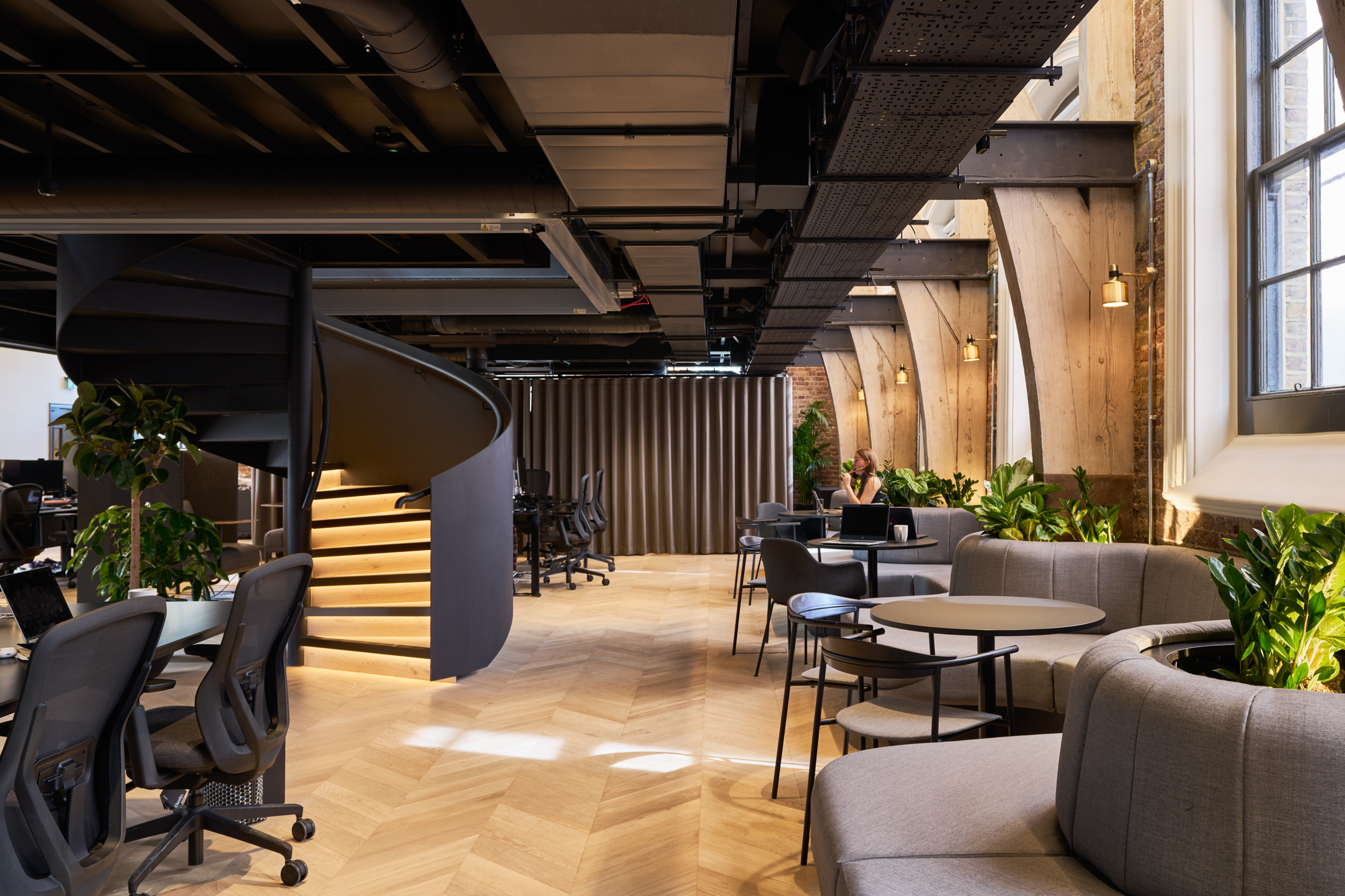 Lotus's office space designed by Modus, showcasing a spiral staircase, open workspaces, and natural wood tones, in the renovated Ragged School building.