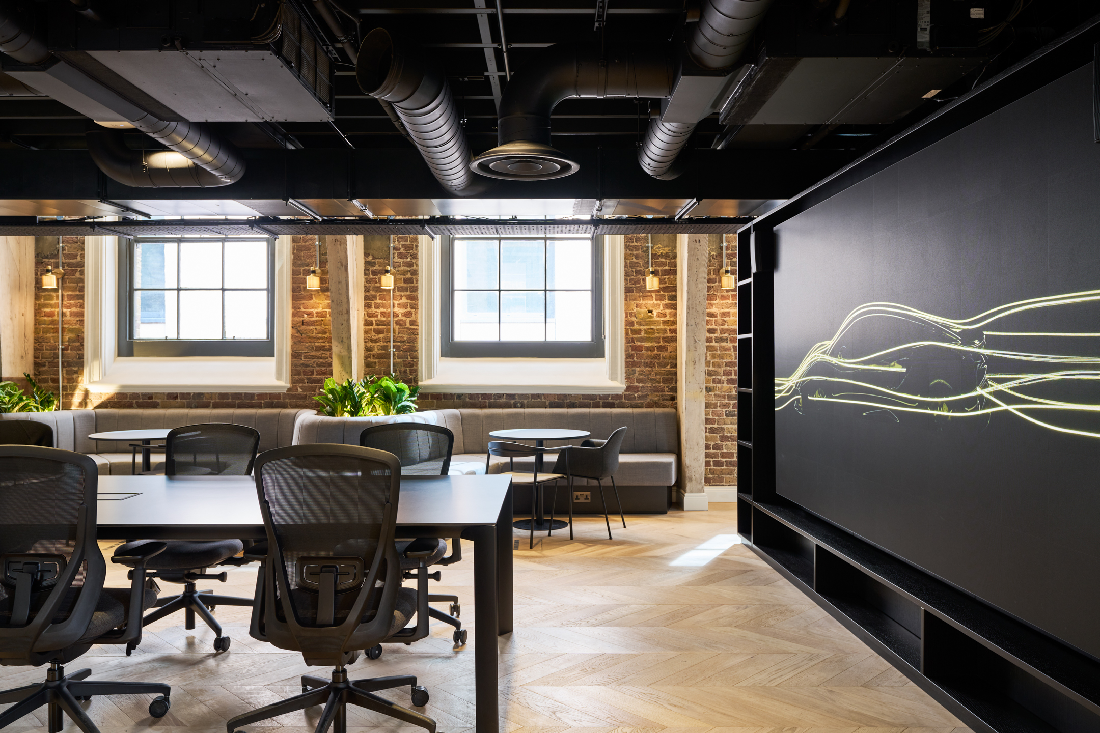 An open meeting area in Lotus’s headquarters, designed by Modus, featuring flexible seating and a sleek digital display, blending modern design with the historic Ragged School structure.