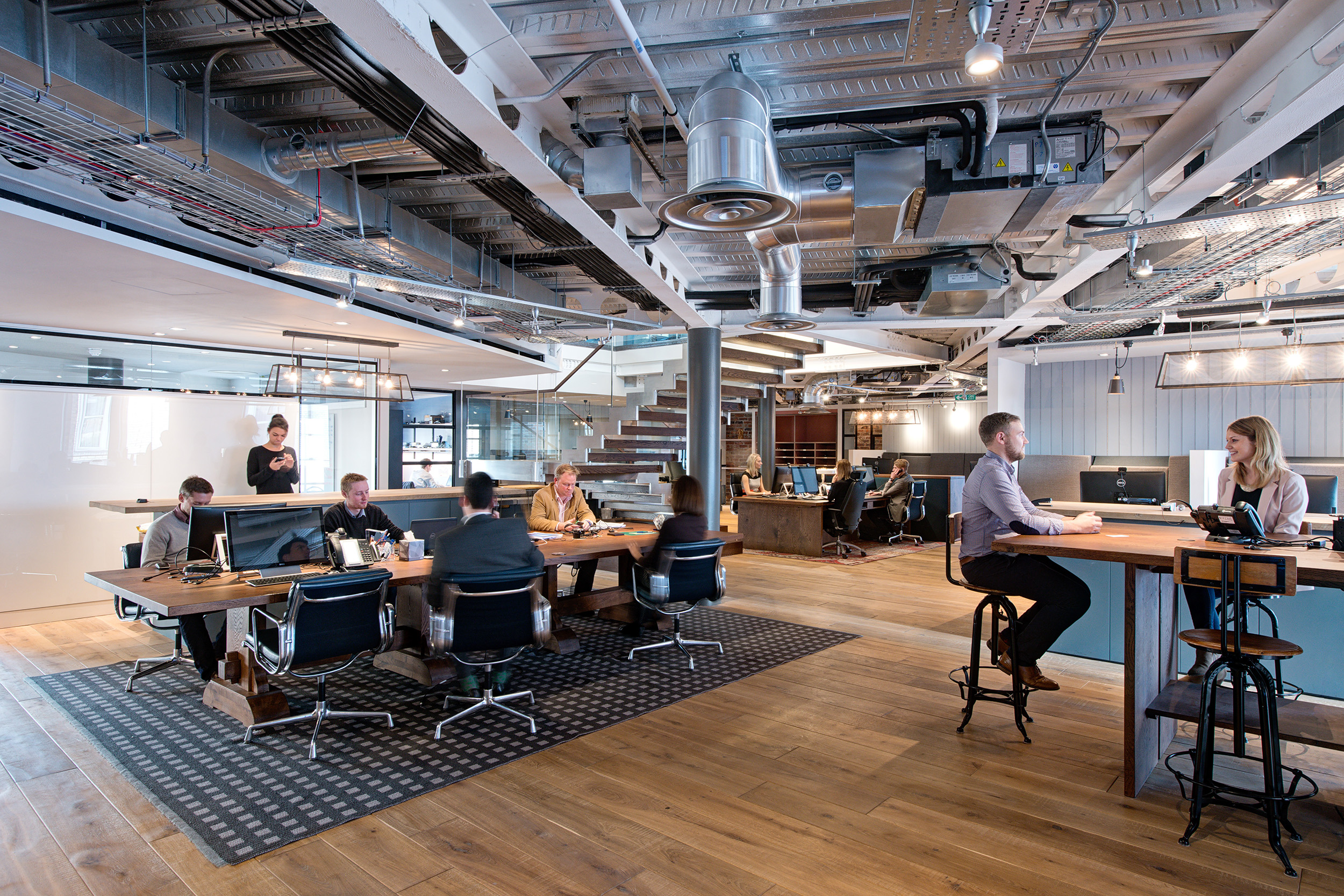 Open-plan collaborative workspace with various seating arrangements and exposed ceilings, showcasing the industrial-style design for the private equity firm.