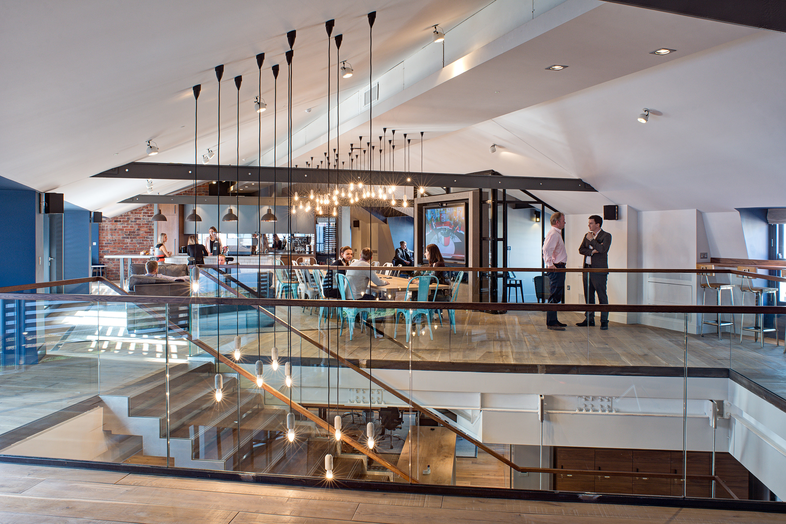 Upper-level teapoint space with a glass railing, large meeting table, and pendant lighting at the private equity firm office.