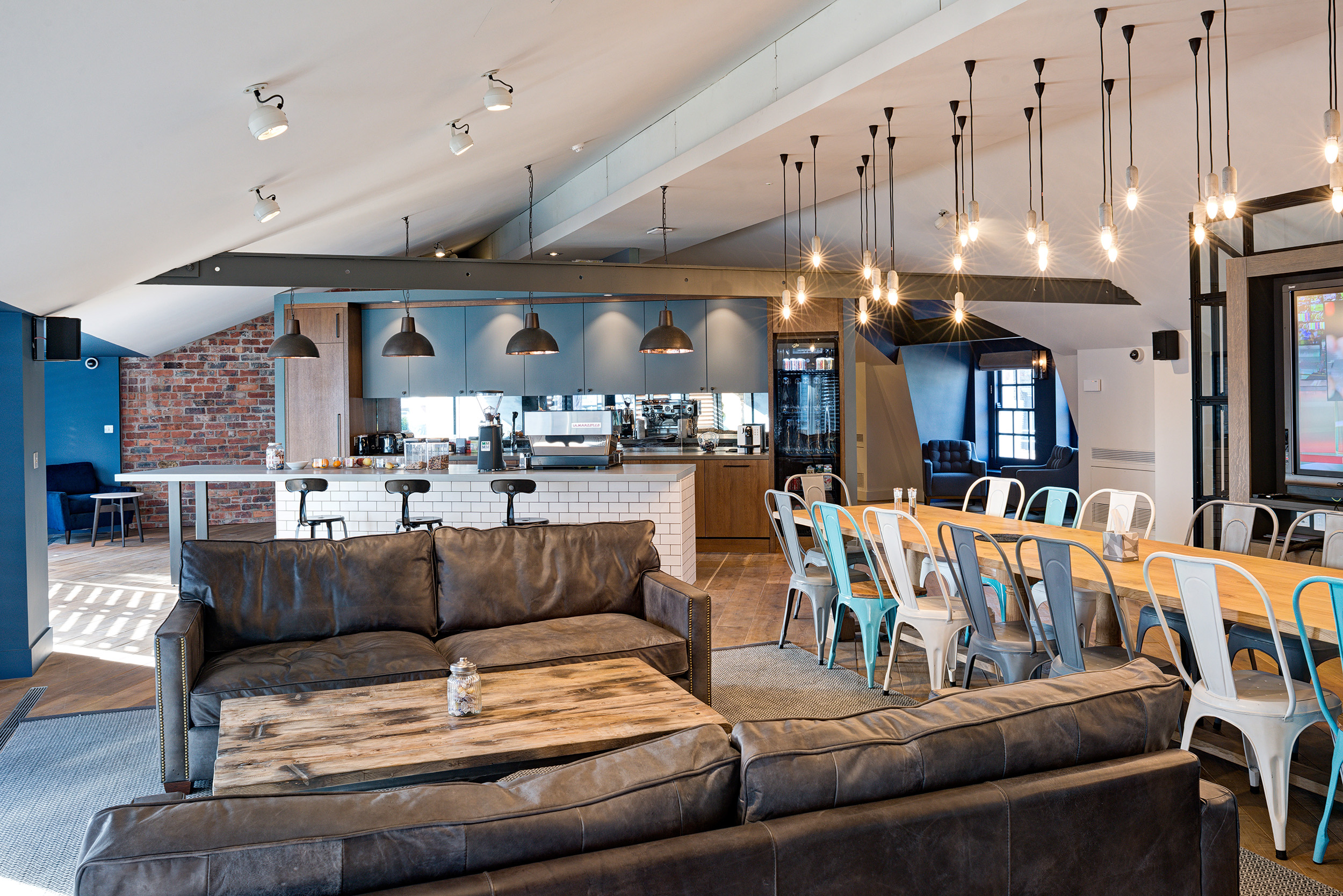 Teapoint area with industrial-style lighting, a large communal table, and modern finishes at the private equity firm’s office.