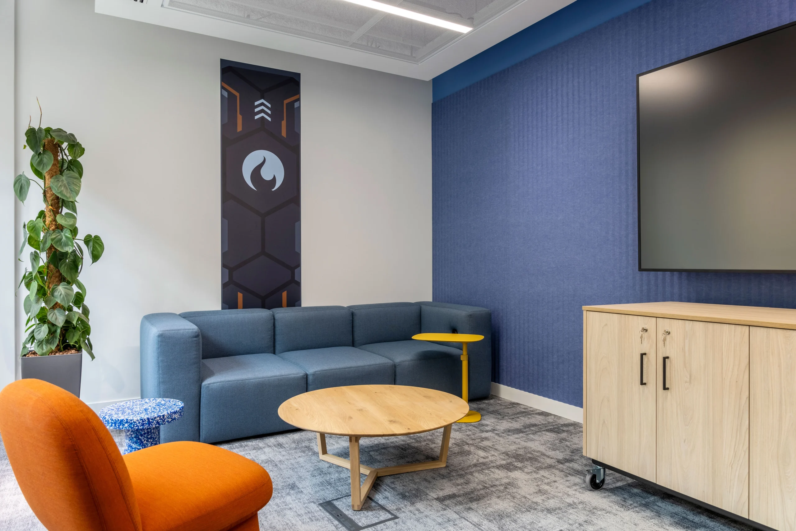 CCP Games' breakout area featuring a blue sofa, orange chair, yellow side table, and vibrant wall graphics, creating a relaxed collaborative space.