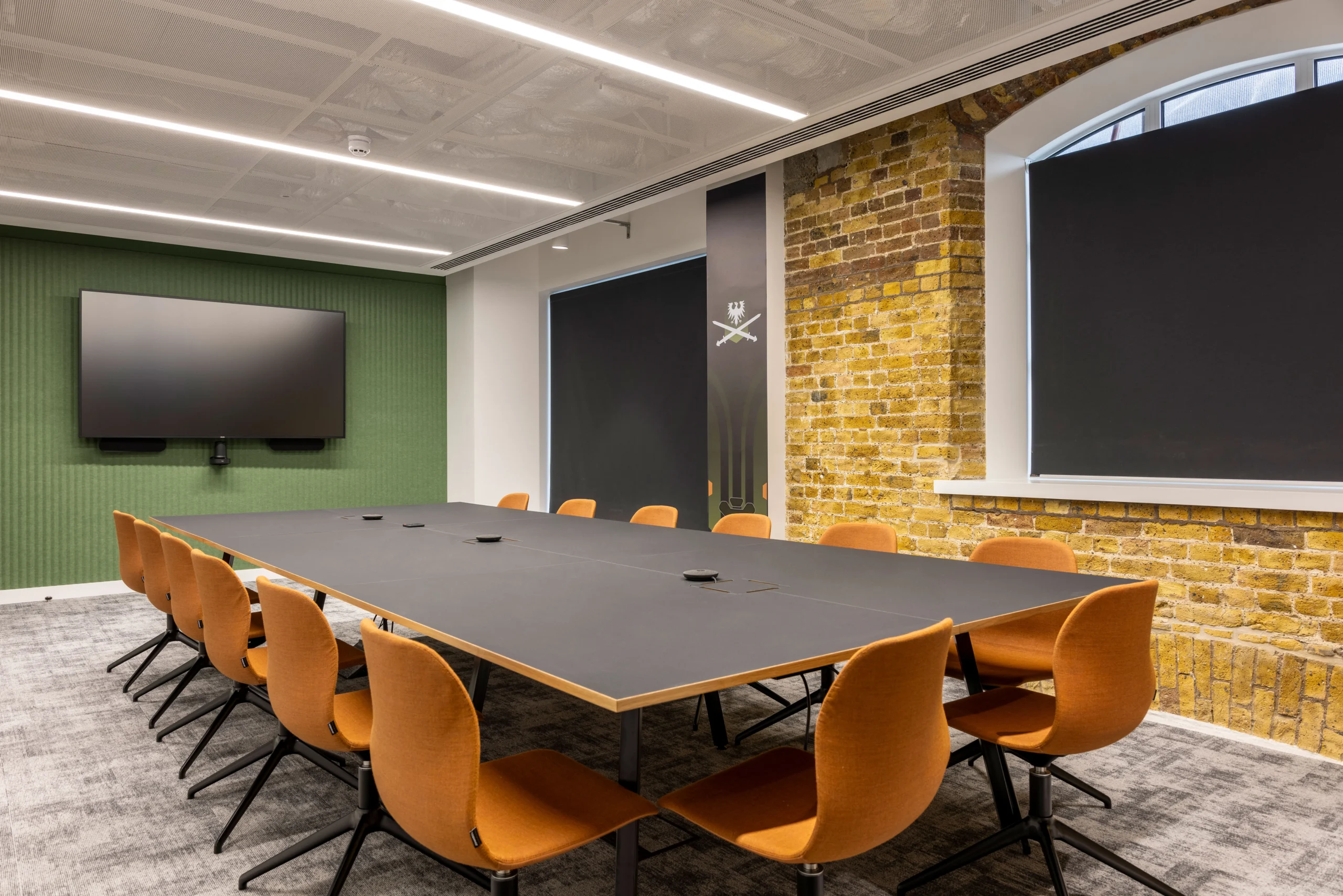 CCP Games' meeting room with orange chairs, a sleek black table, exposed brick walls, and a mounted screen, blending modernity with industrial charm.