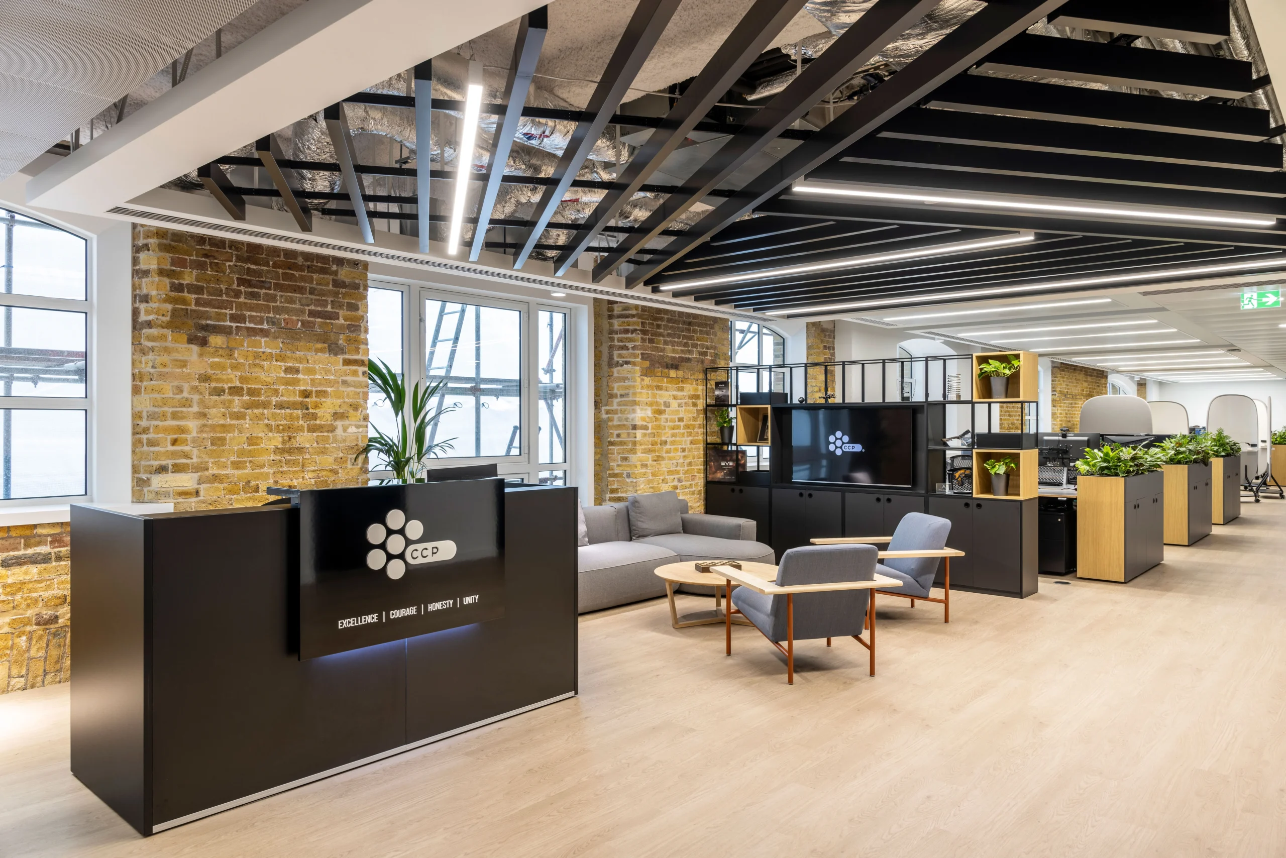 CCP Games reception area featuring a black desk with illuminated branding, exposed brick walls, and modern furnishings with greenery accents.