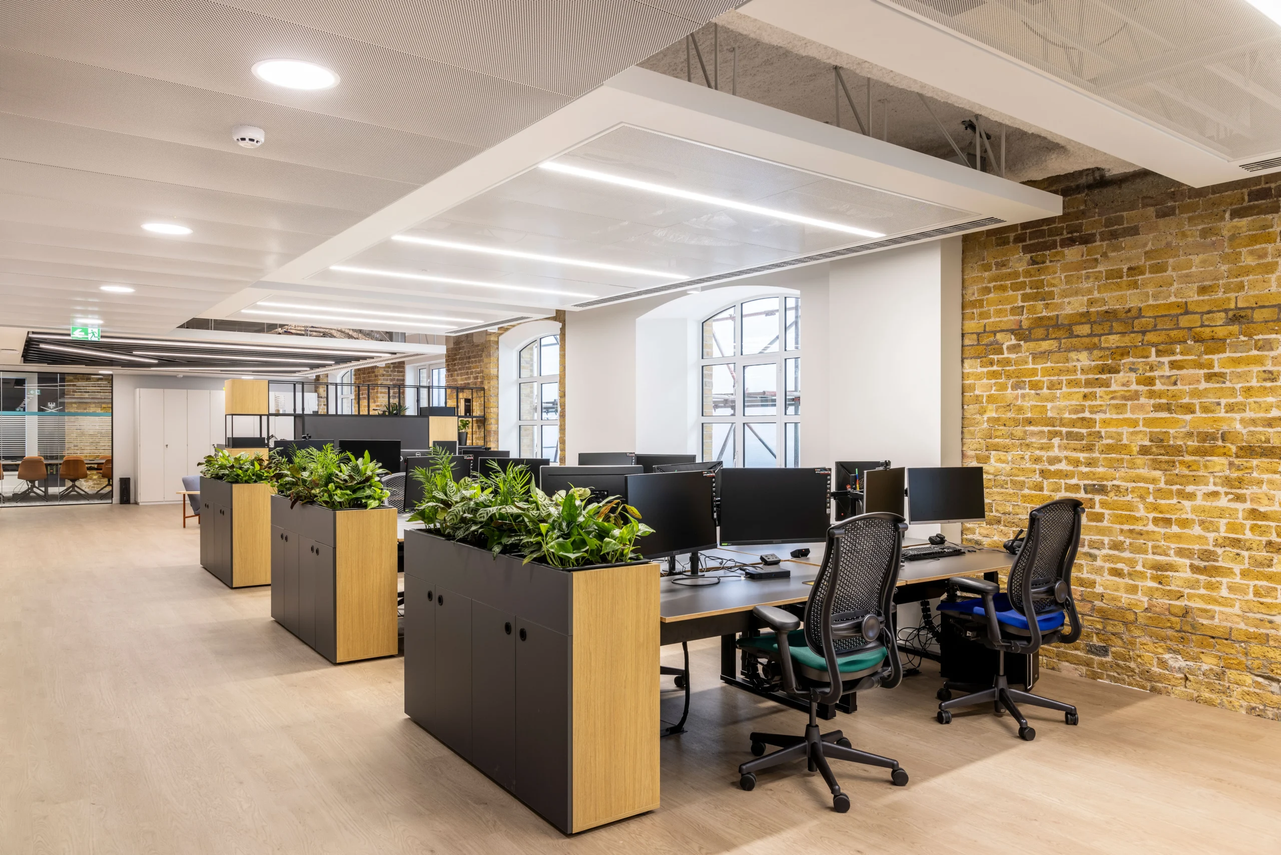 CCP Games open-plan workspace with modern desks, ergonomic chairs, planters for added greenery, and exposed brick walls under a sleek ceiling design.