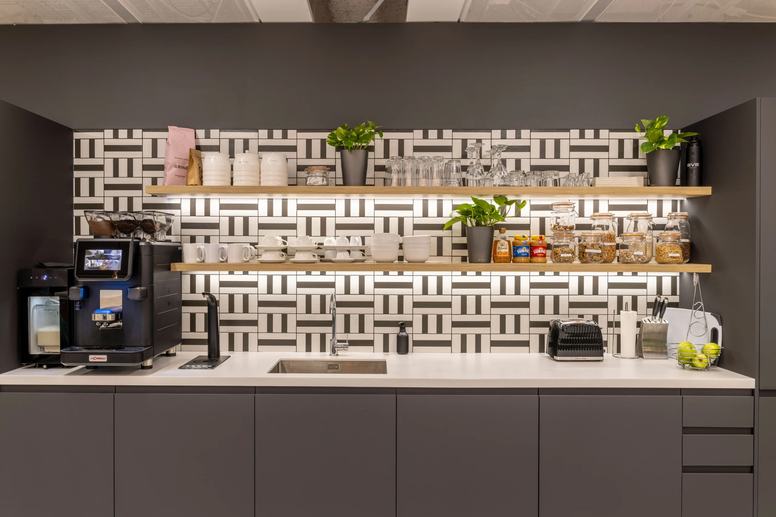 Modern teapoint at CCP Games' London office featuring sleek shelving, patterned tiles, and a variety of refreshments.