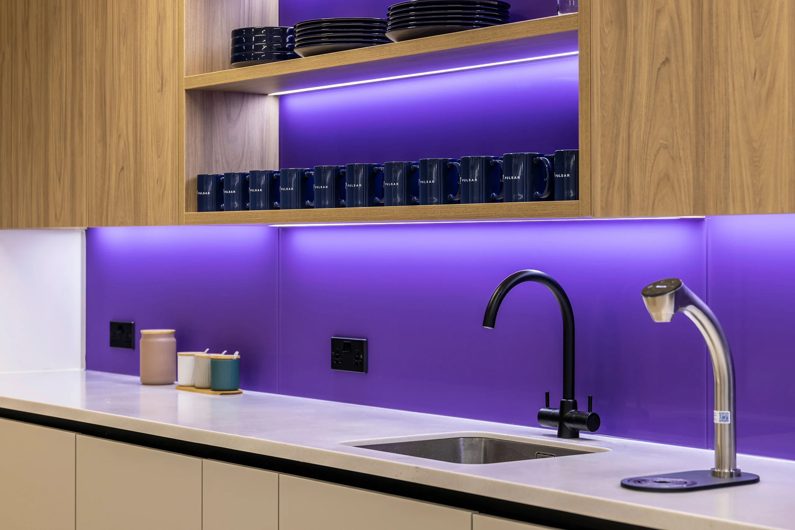 Close-up of the teapoint at Pulsar’s HQ, featuring sleek cabinetry, a bold purple backsplash, and stylish black and silver taps.