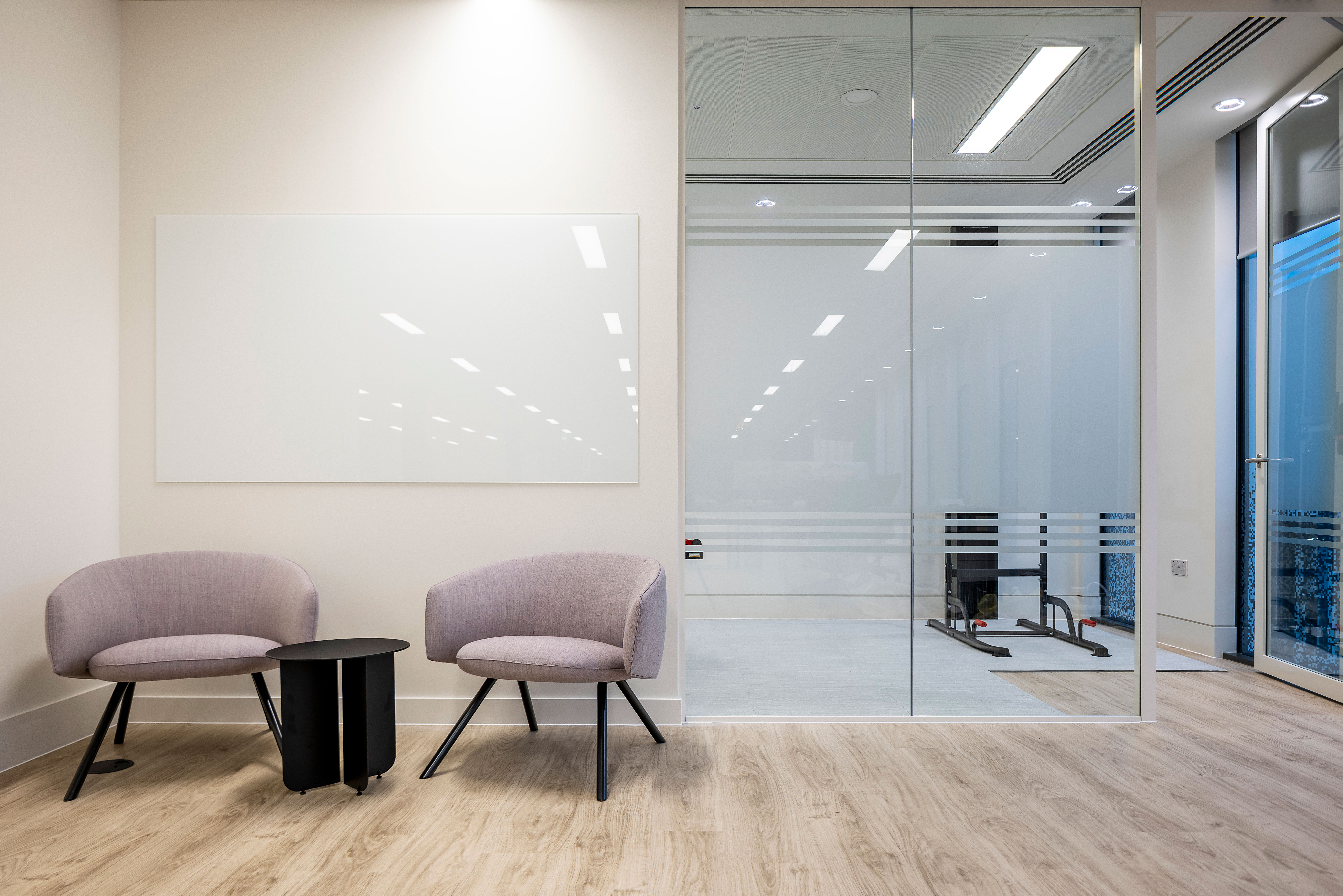 Minimalist breakout area at Pulsar’s London HQ, featuring modern chairs, a sleek black table, and glazing partitions for a clean, professional look.